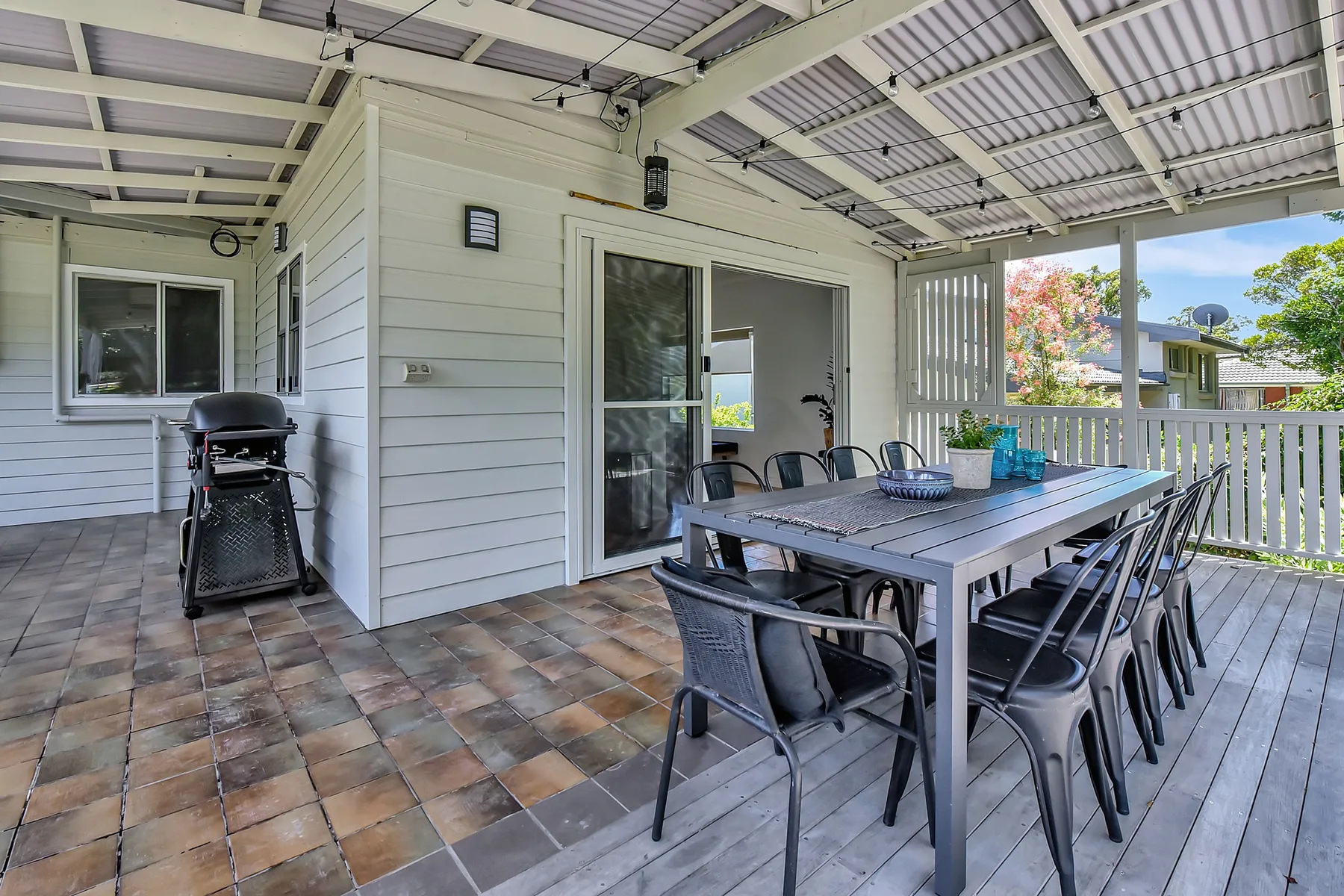 A covered outdoor dining area with a table and seating beside a barbecue.