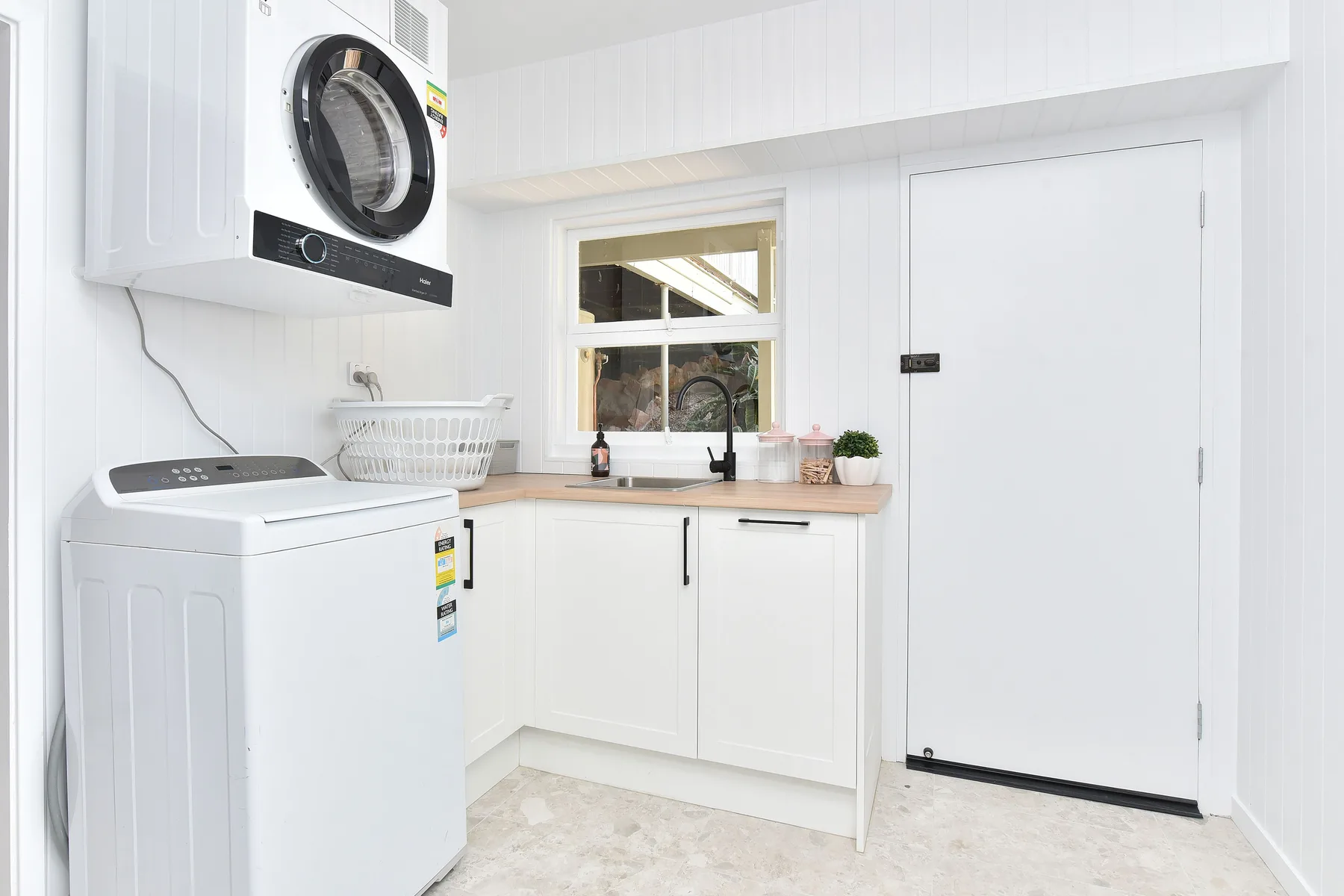 A bright laundry room with a washer, dryer, and white cabinetry.