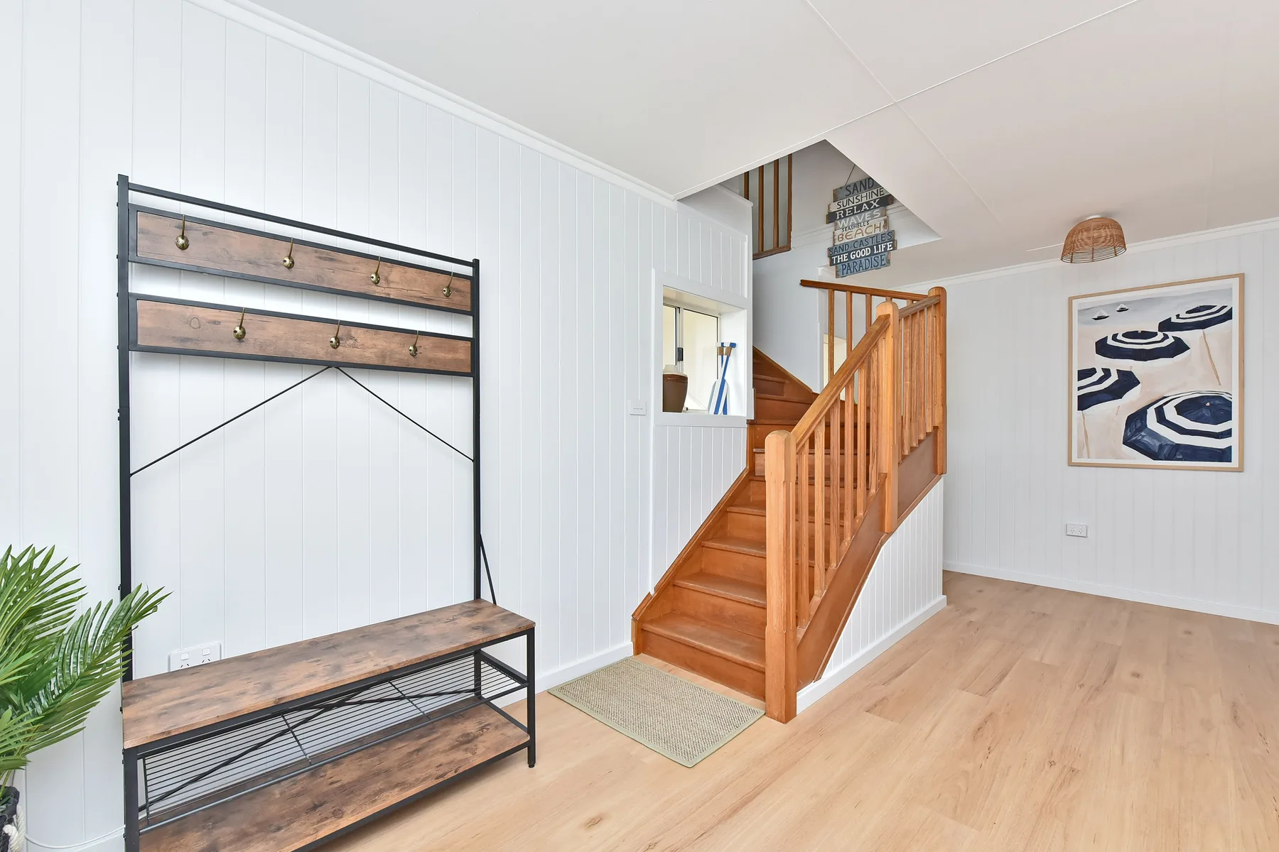 A bright entryway features a wooden staircase and a bench beneath a wall-mounted coat rack.