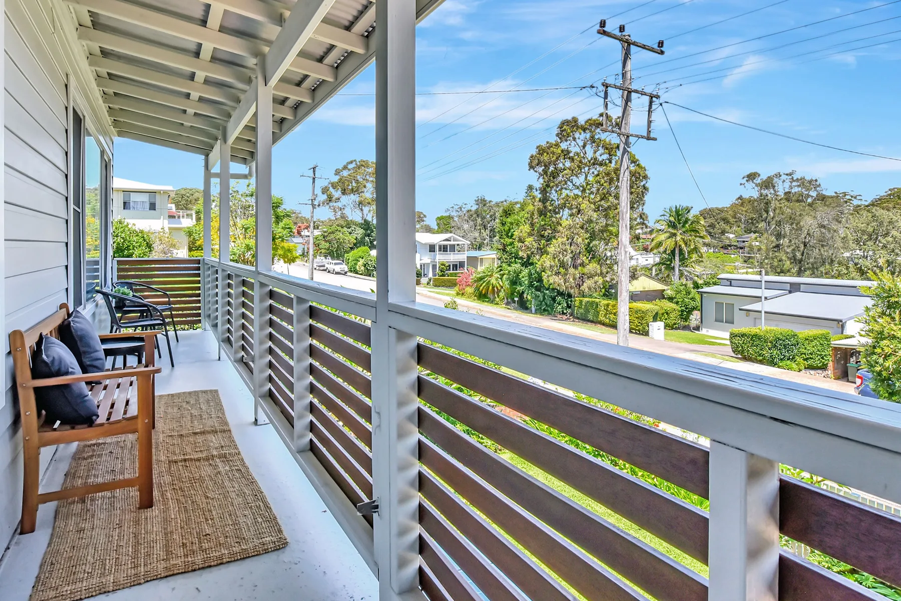 Covered porch with wooden seating overlooking a leafy residential street.