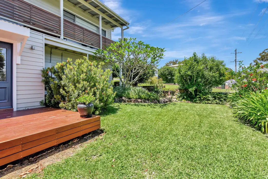 A grassy garden beside a house, with a wooden deck and leafy shrubs.