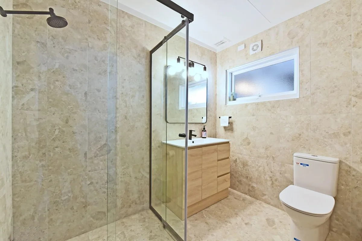 A tiled bathroom with a glass shower, vanity, and toilet.