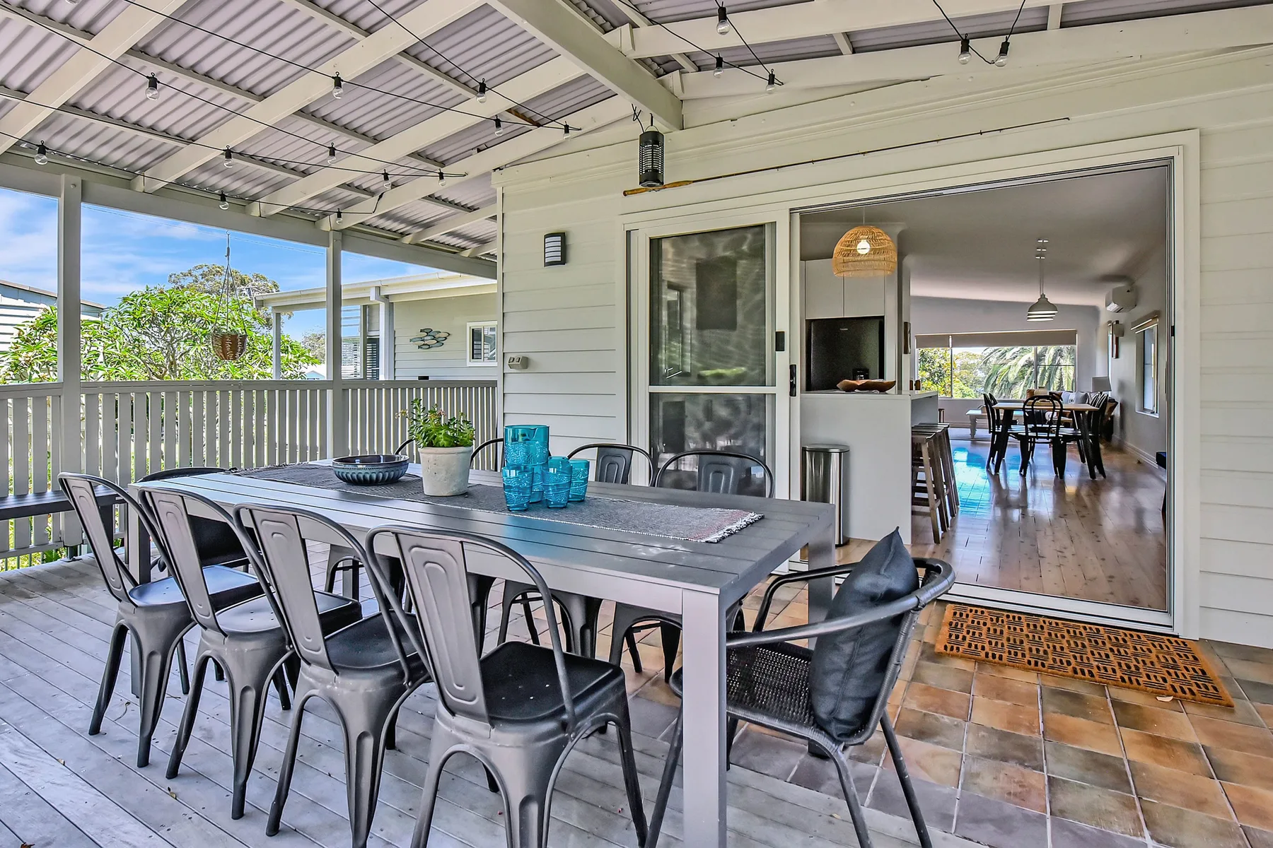 A covered outdoor dining area with a table and chairs beside open doors.