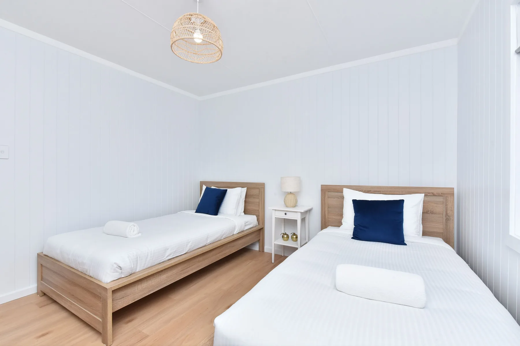 A bright bedroom with two beds, white bedding, and blue accent pillows.