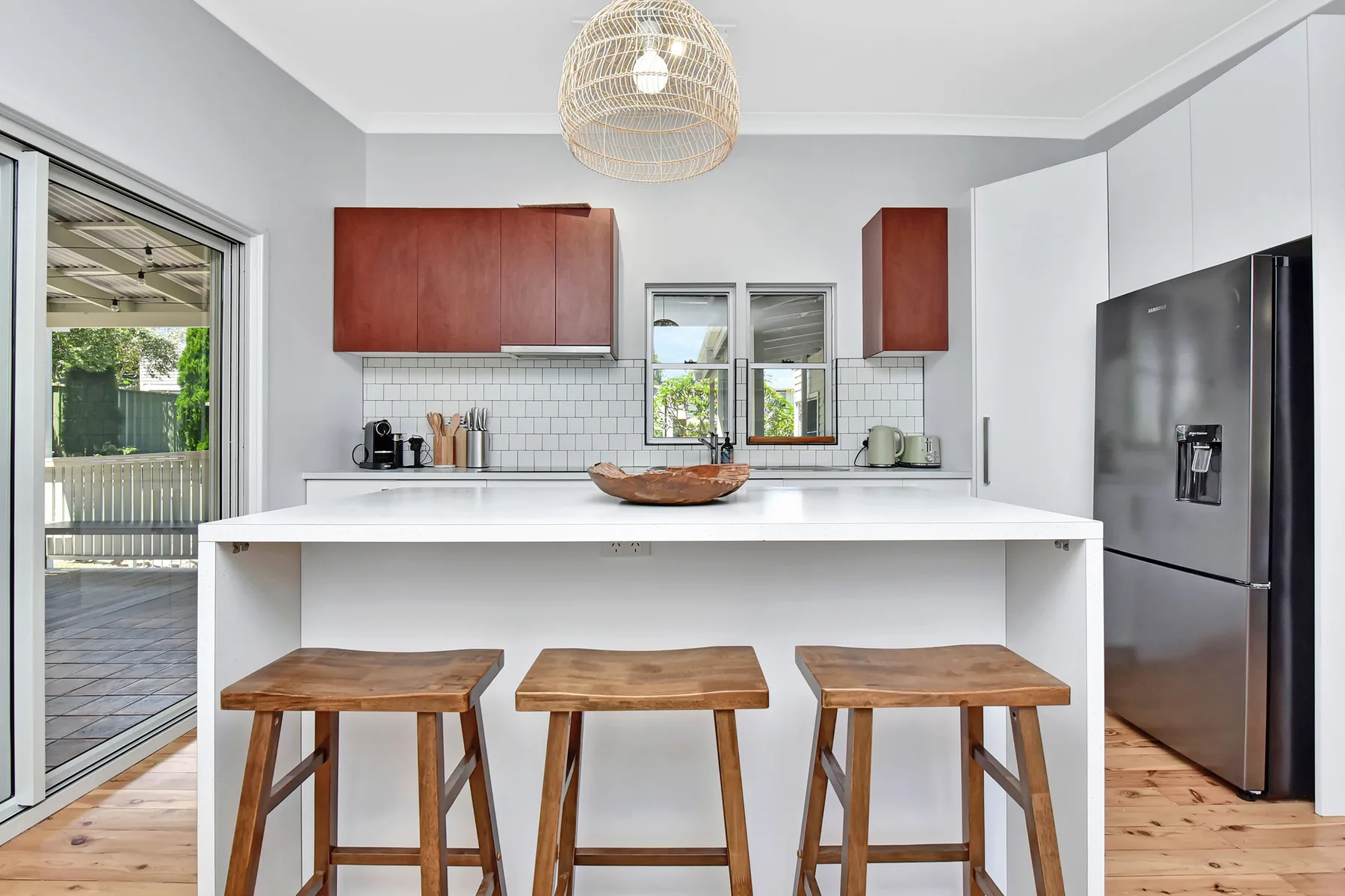 A bright kitchen with a wide island, wooden stools, and a refrigerator.