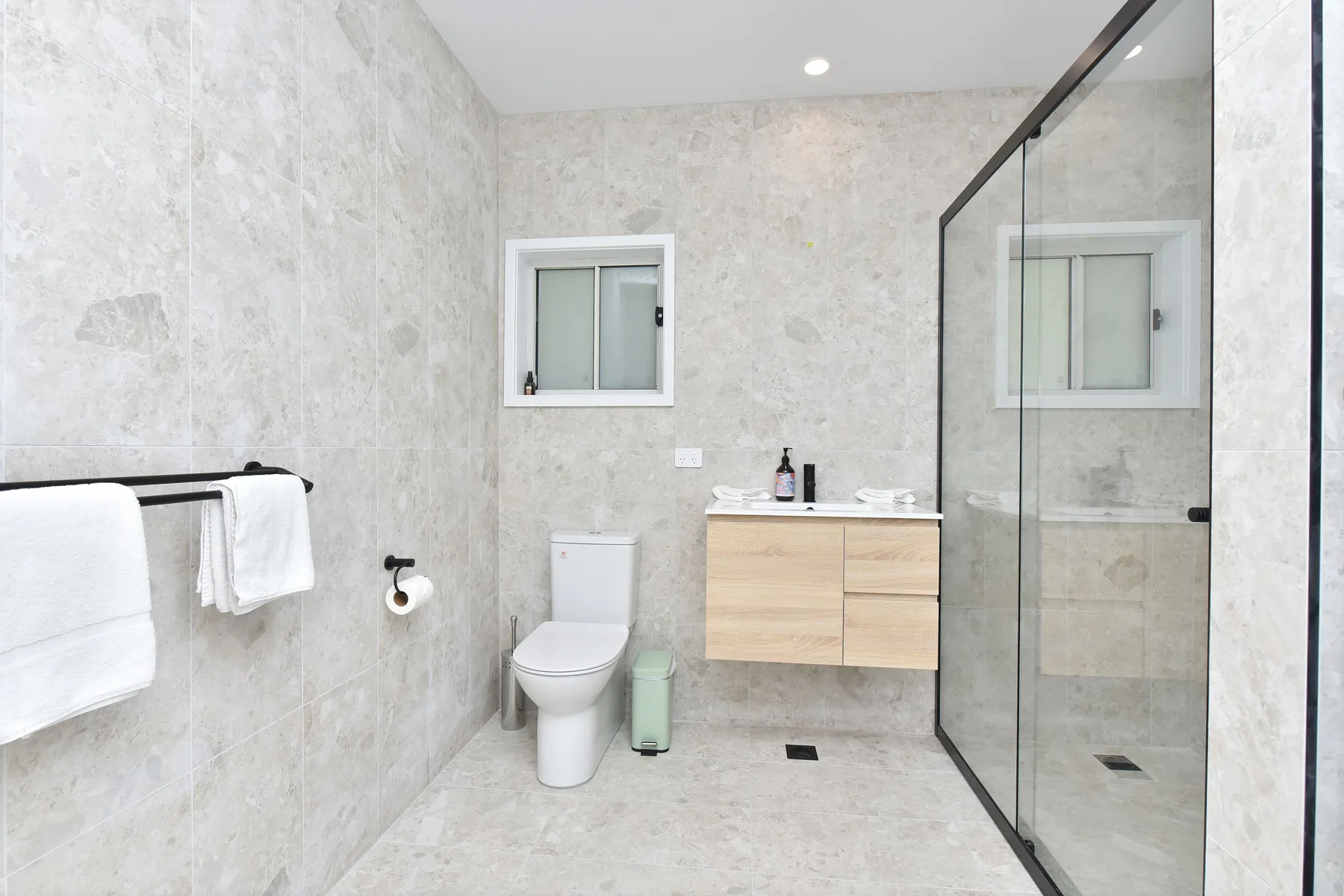 A tiled bathroom with a vanity, toilet, and glass shower.