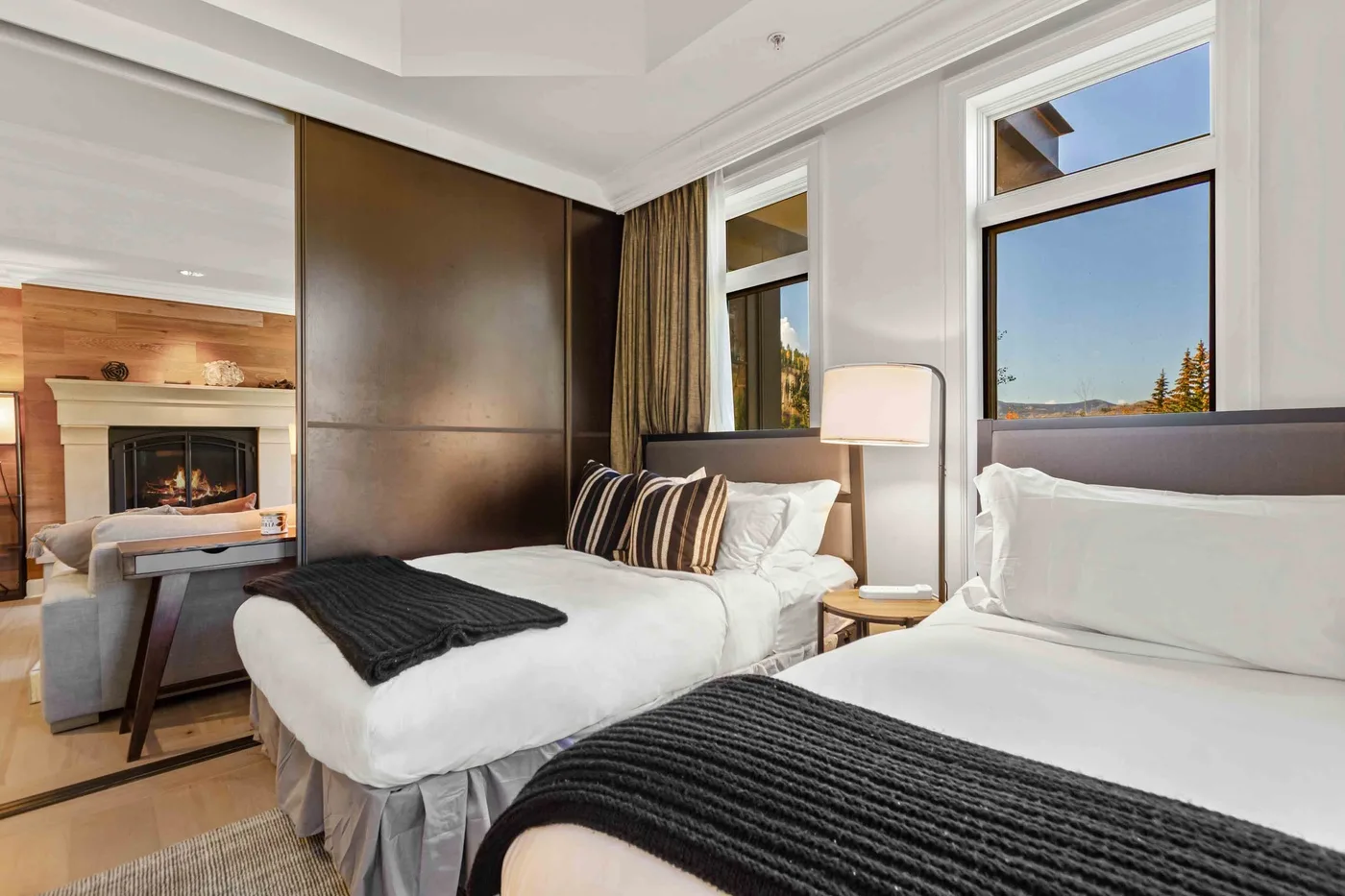 Un dormitorio luminoso con dos camas, ropa de cama blanca y ventanas altas.