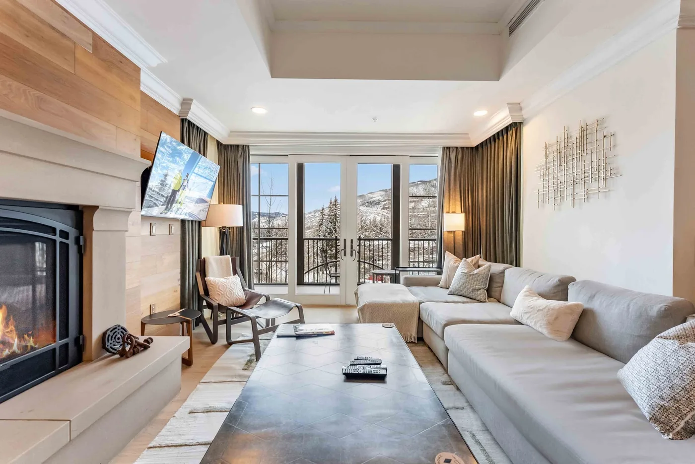 A bright living room with a fireplace, seating, and glass doors overlooking snowy trees.