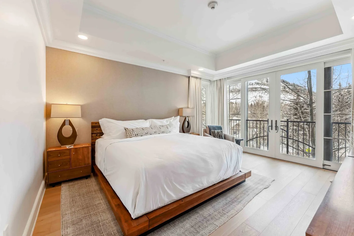 Un dormitorio luminoso con una cama grande junto a ventanales con vistas a los árboles.