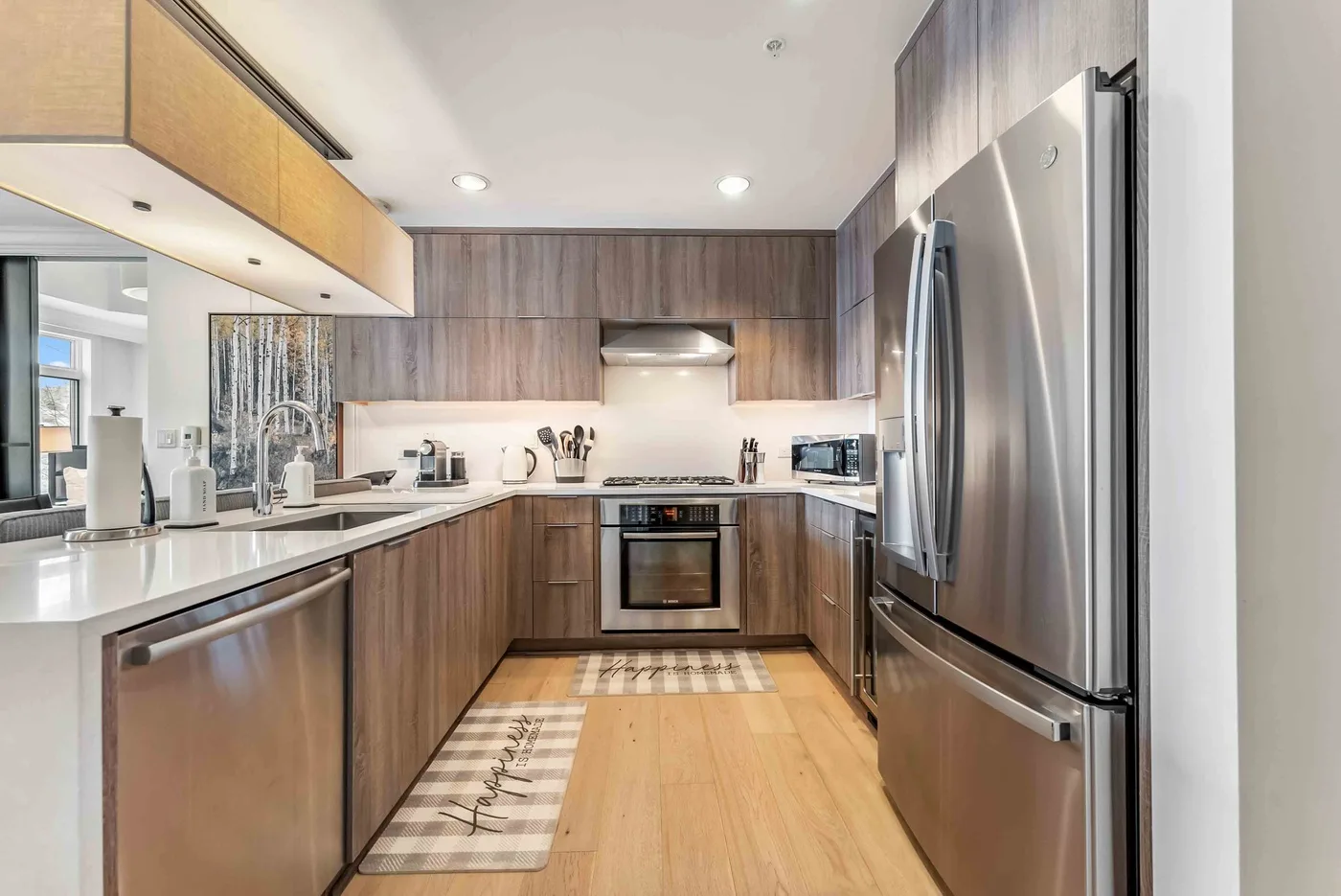 A modern kitchen with wood cabinetry, white counters, and stainless steel appliances.