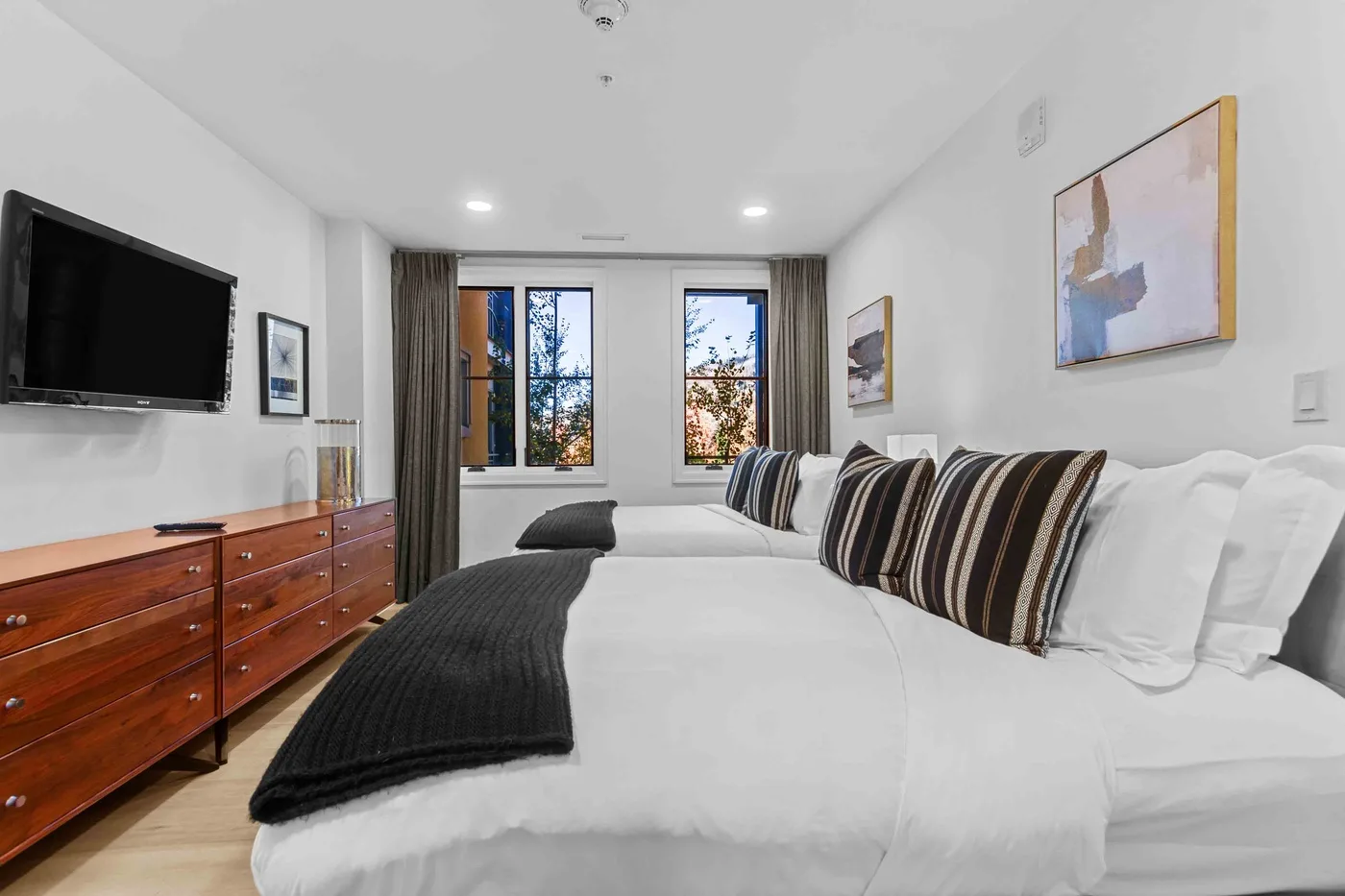 Un dormitorio con camas tendidas, almohadas a rayas y una cómoda de madera.