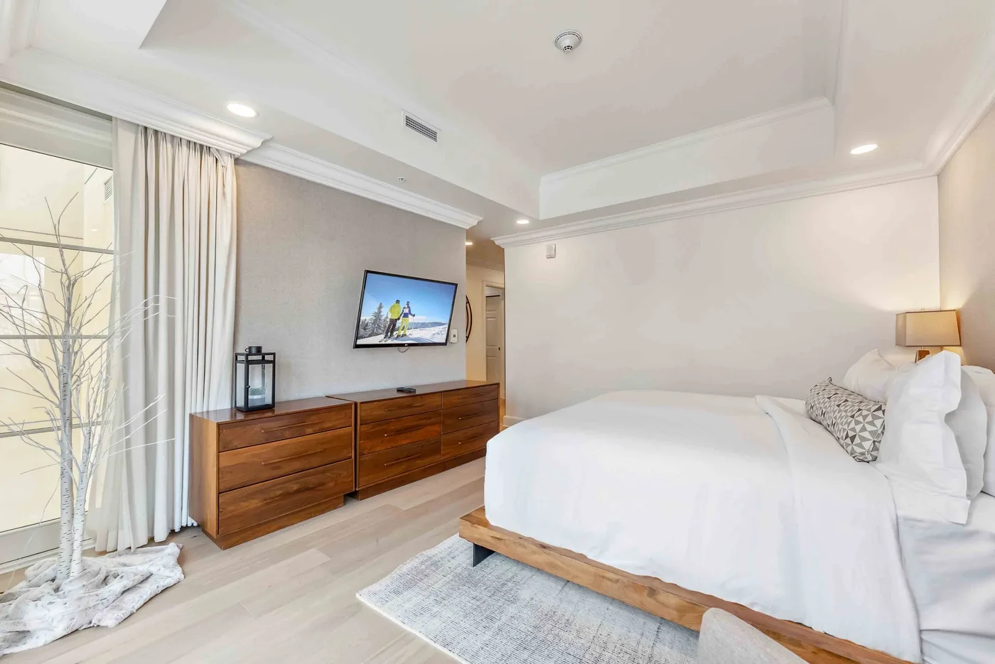 Un dormitorio luminoso con una cama bien hecha y un televisor sobre una cómoda.