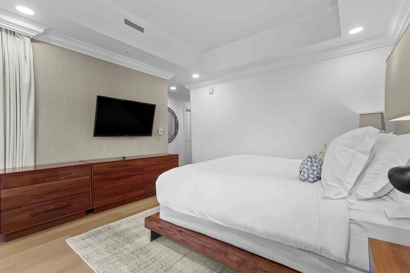 Un dormitorio con una cama grande, un televisor en la pared y una cómoda de madera.
