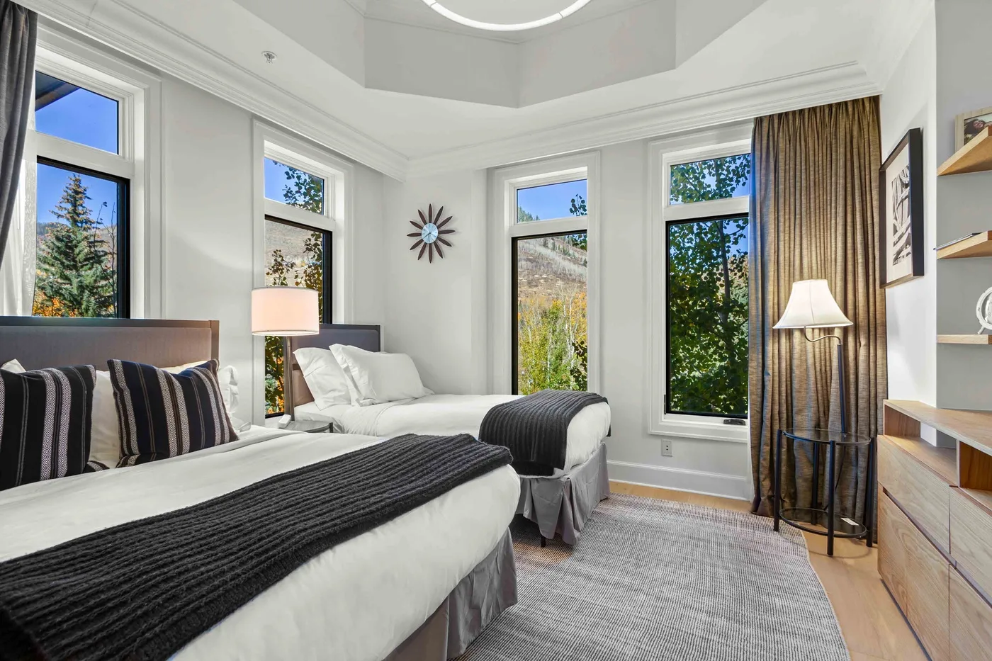 Un dormitorio luminoso con dos camas, ventanas grandes y una alfombra gris.