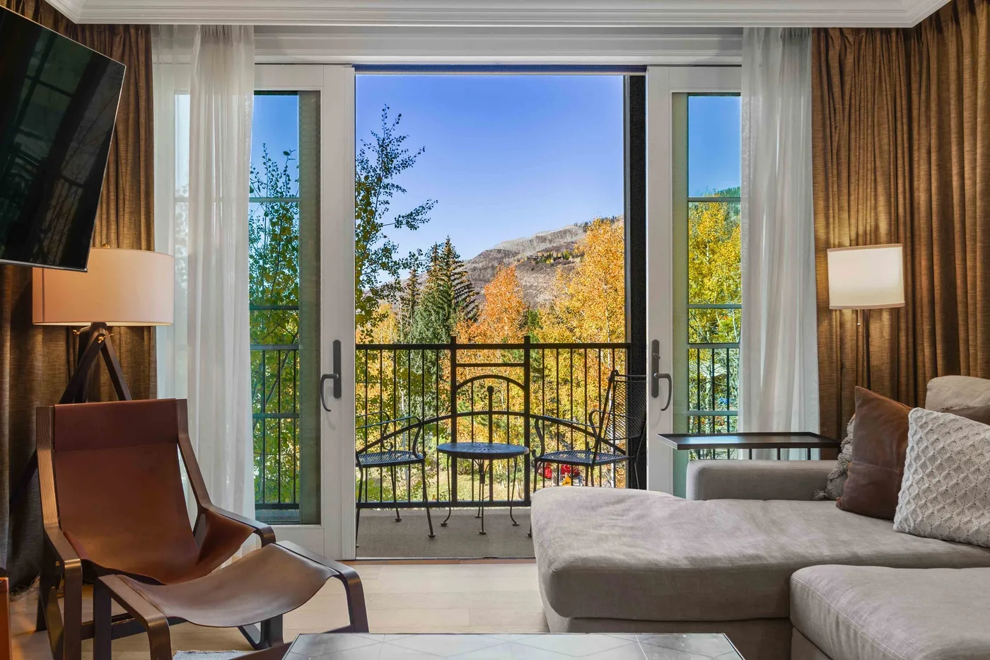 Una sala de estar con asientos junto a grandes ventanales con vistas a árboles otoñales.