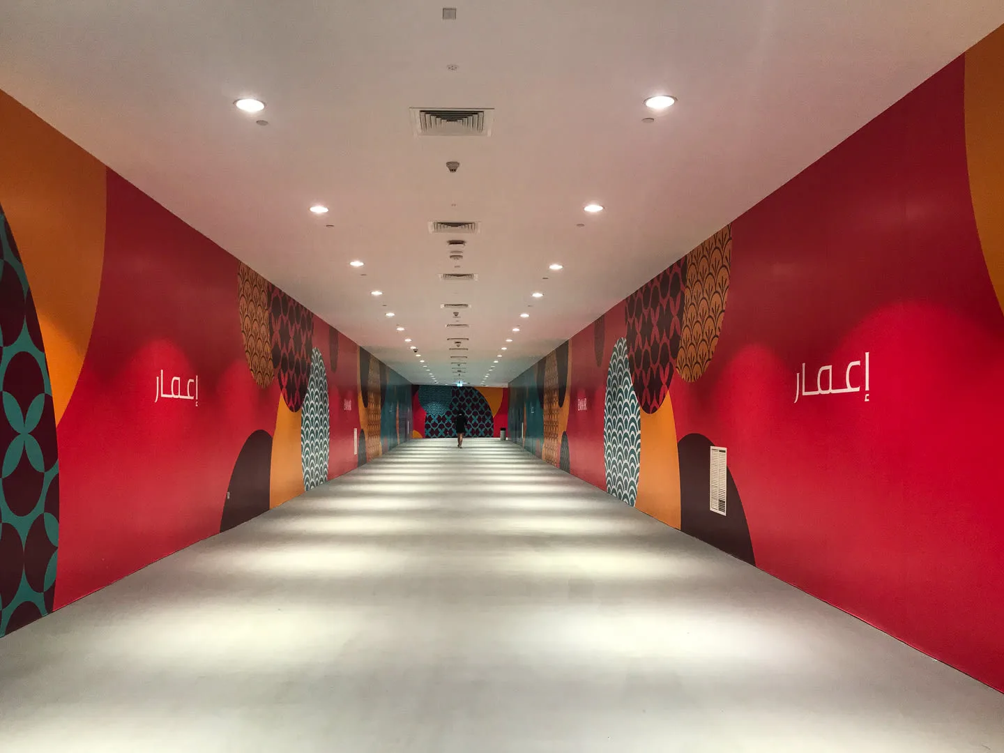 Un largo pasillo interior tiene paredes coloridas con diseños y un suelo bien iluminado.