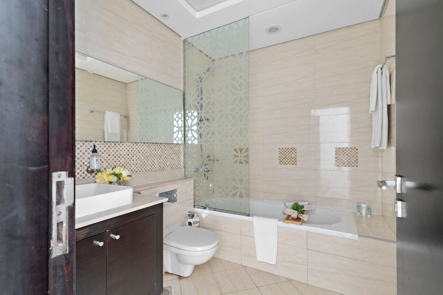Un baño de azulejos con bañera, mampara de vidrio y lavabo.