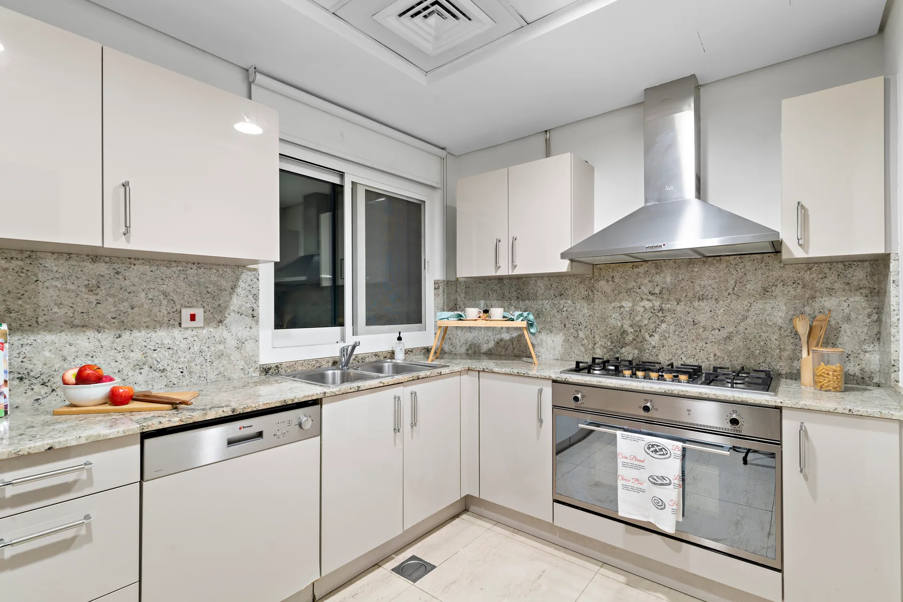 Una cocina luminosa con gabinetes blancos, una ventana y una cocina de acero inoxidable.