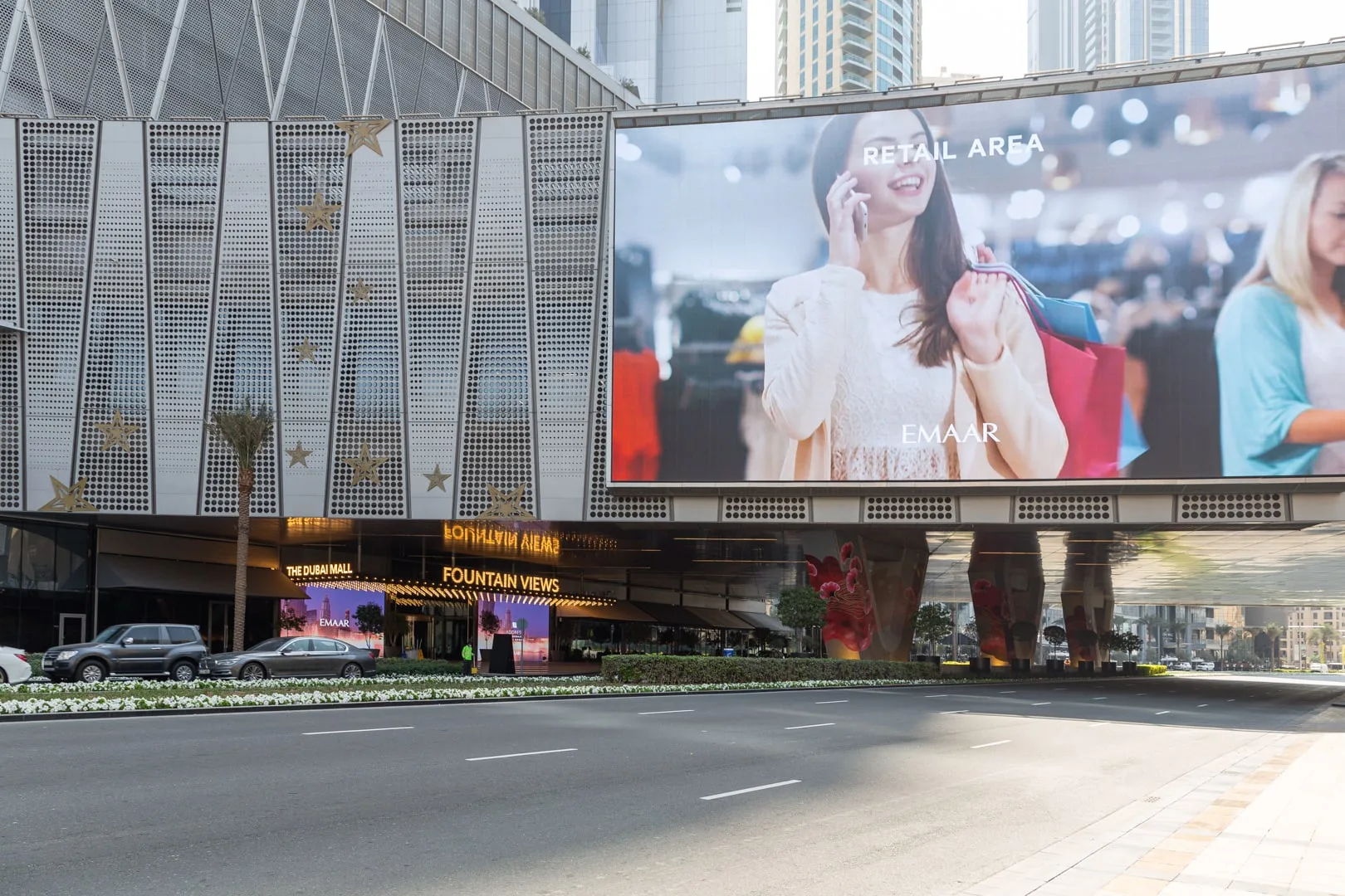 La fachada de un centro comercial con una gran pantalla digital sobre la carretera.