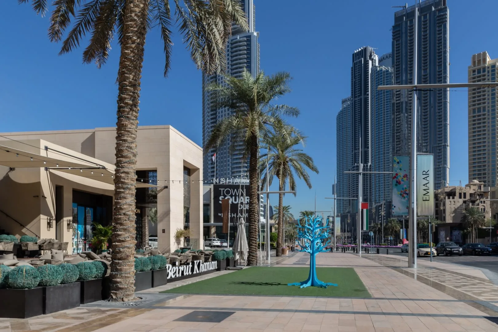 Una plaza peatonal al aire libre con palmeras y edificios altos al fondo.