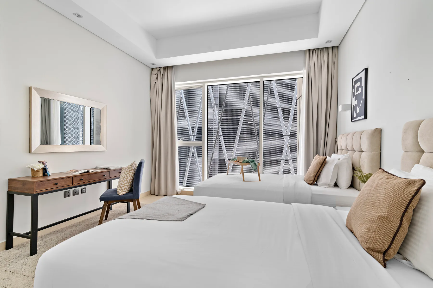 Un dormitorio luminoso con una cama grande, un escritorio y amplias ventanas con cortinas.