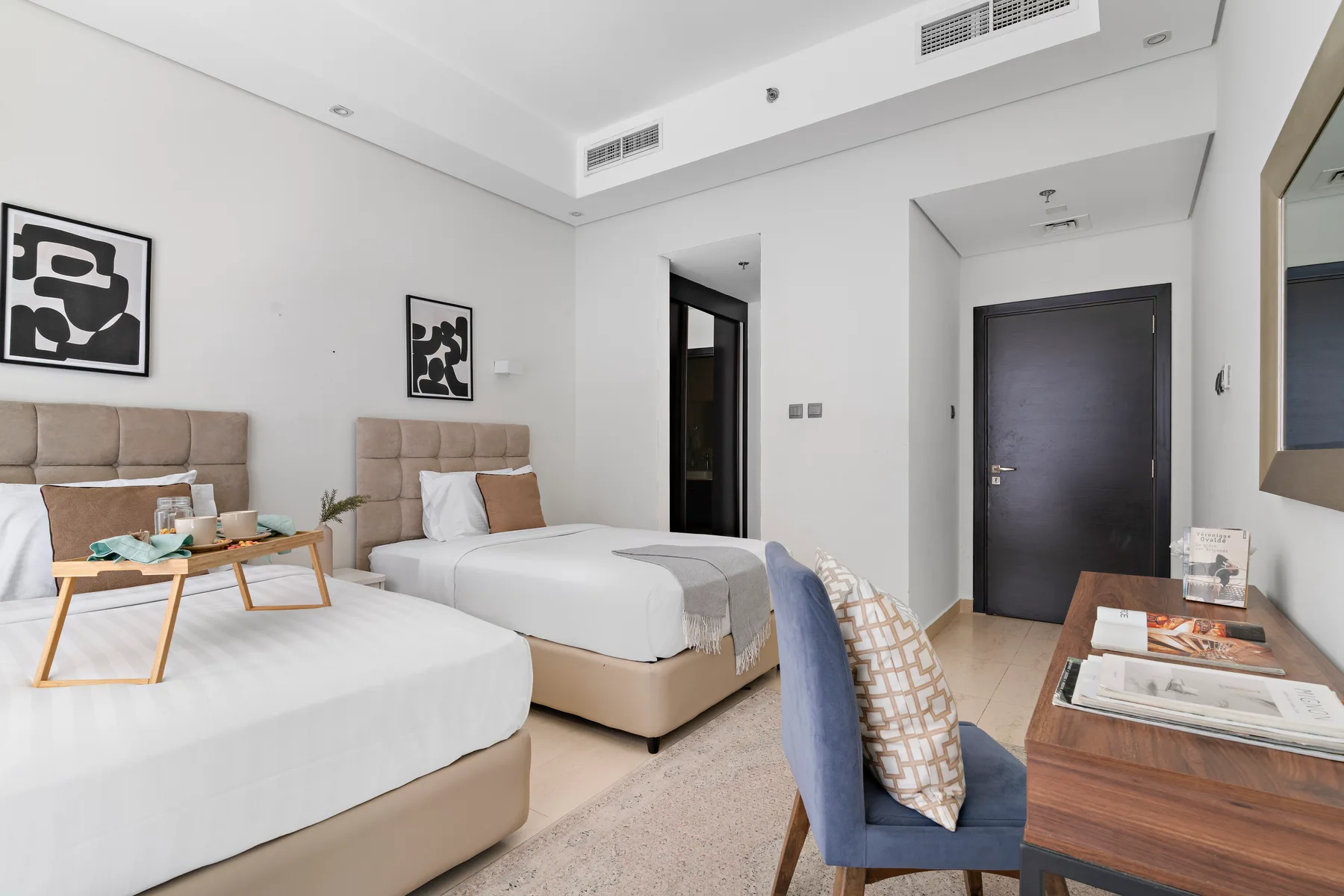 Un dormitorio luminoso con dos camas y una pequeña zona de estar junto a la entrada.