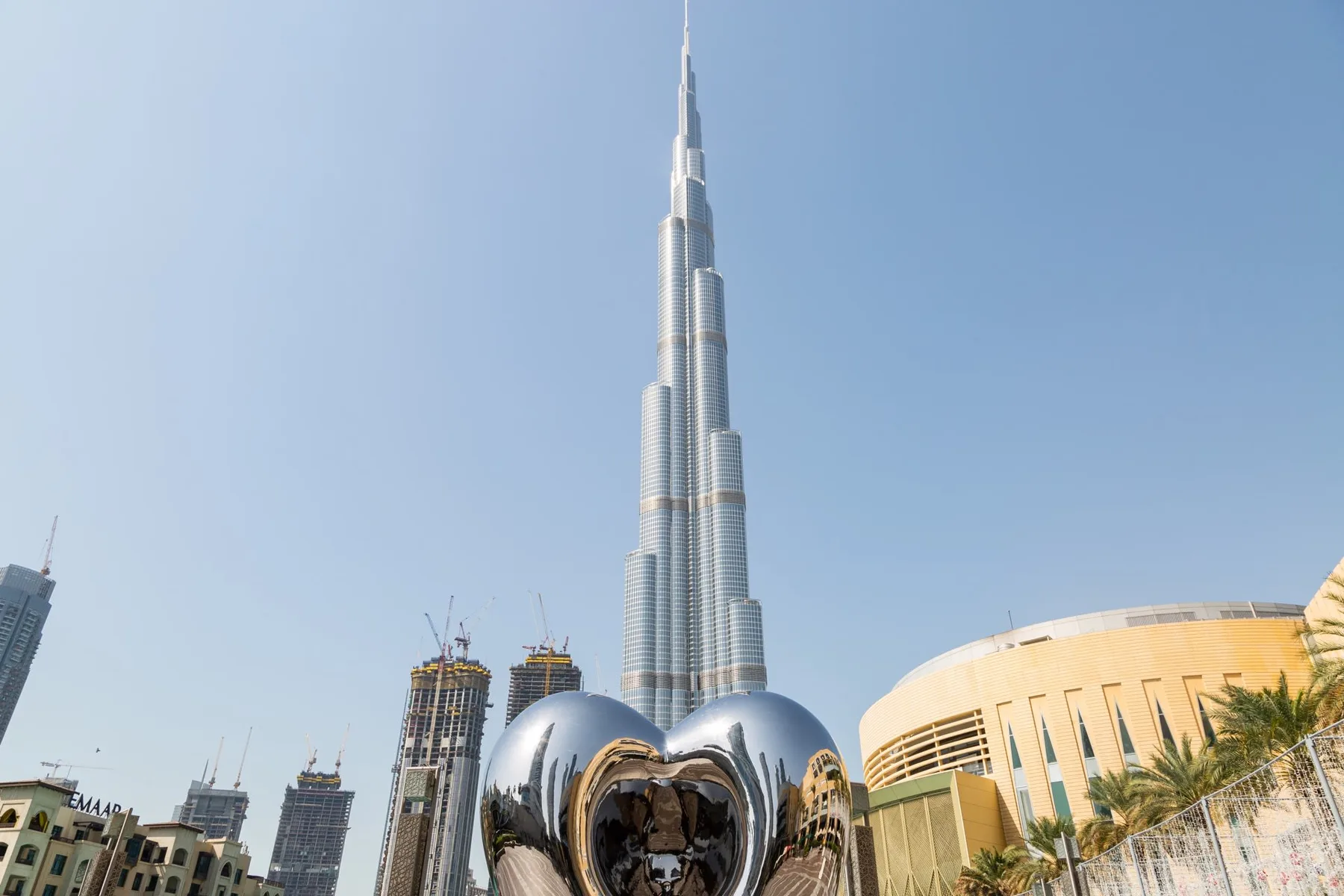 El Burj Khalifa se eleva sobre edificios cercanos junto a una escultura reflectante.