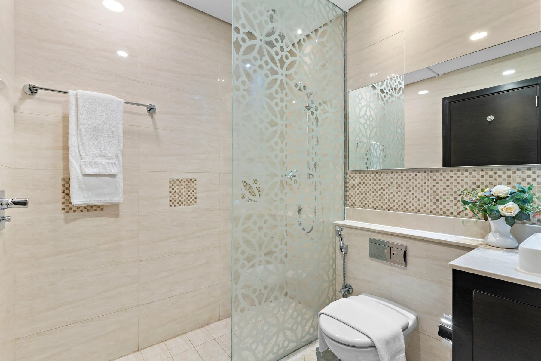 Un baño luminoso con una mampara de ducha de vidrio decorada y un tocador.