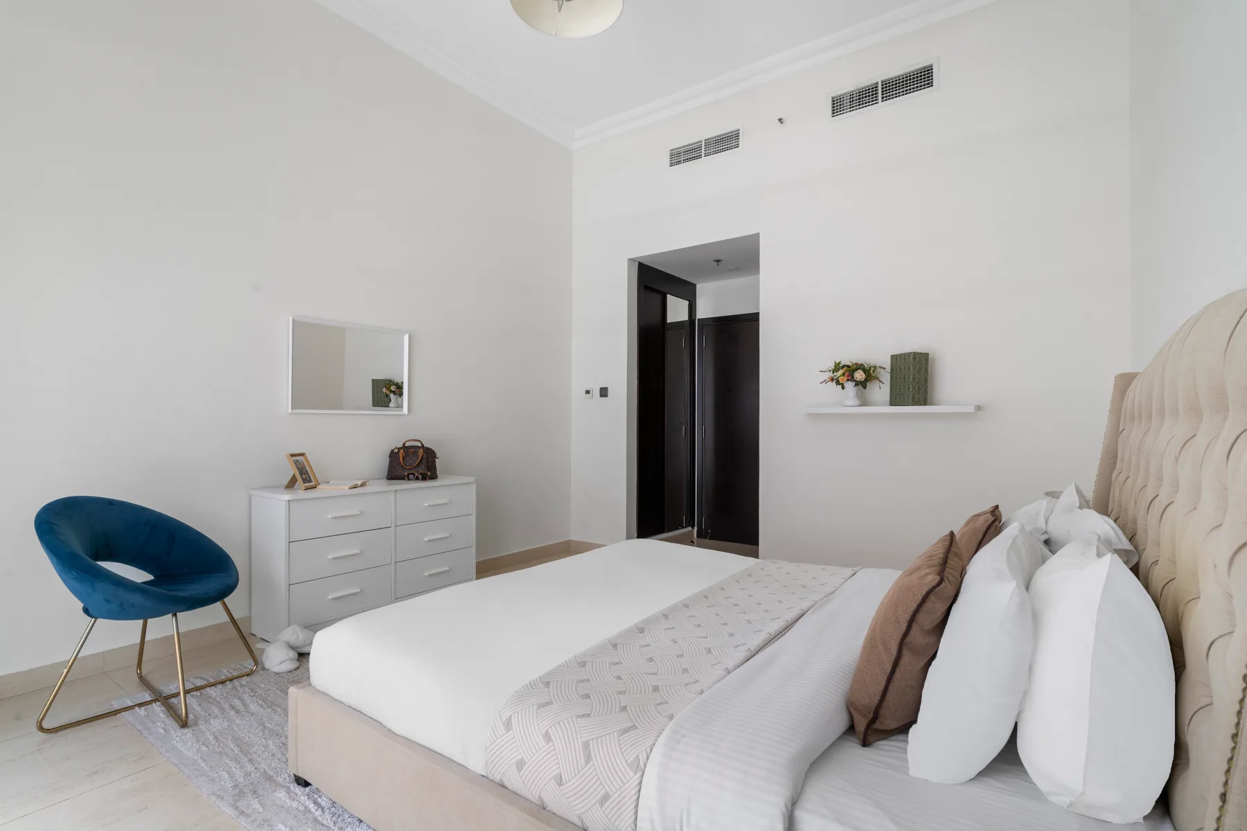Un dormitorio luminoso con cama, cómoda y asiento azul.