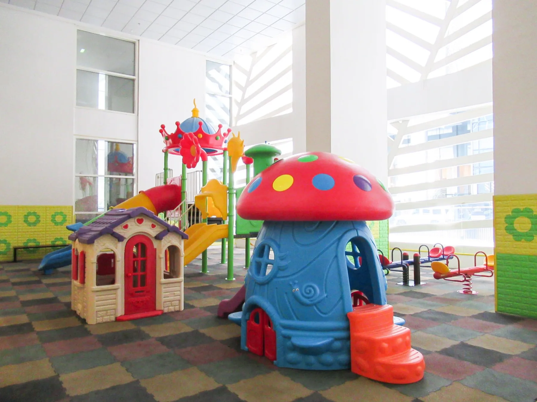 Un área de juegos infantil interior con estructuras coloridas y suelo acolchado.