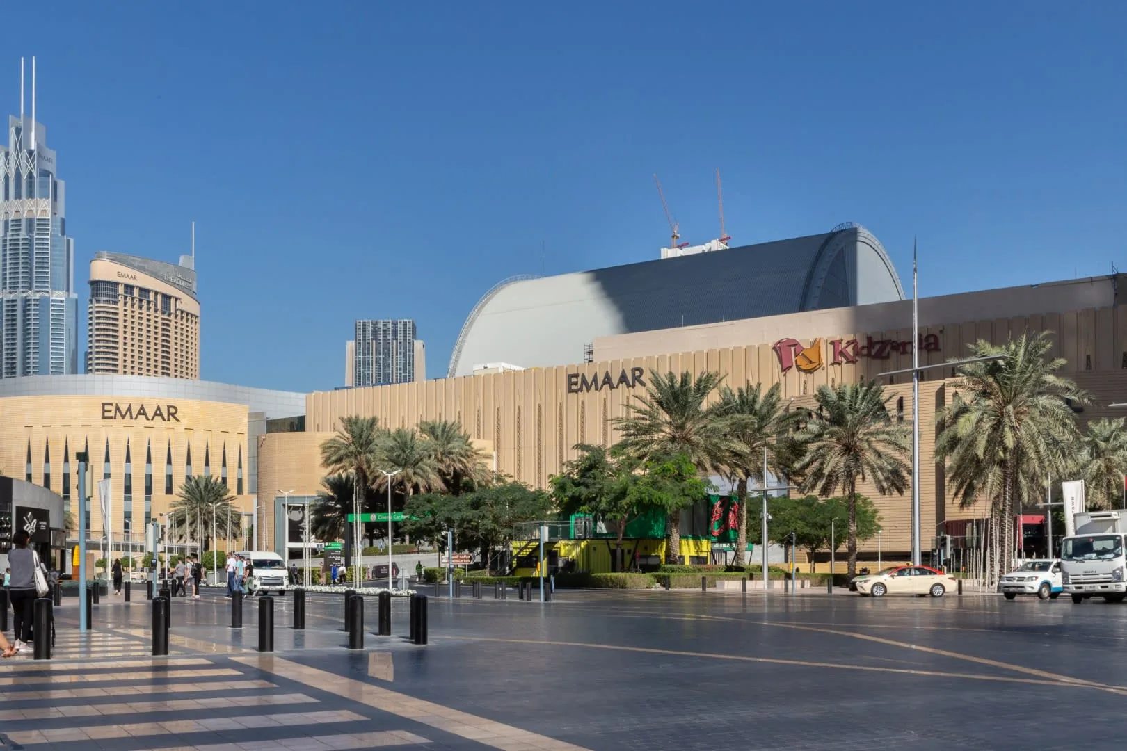 Un centro comercial moderno con palmeras y edificios altos al fondo.