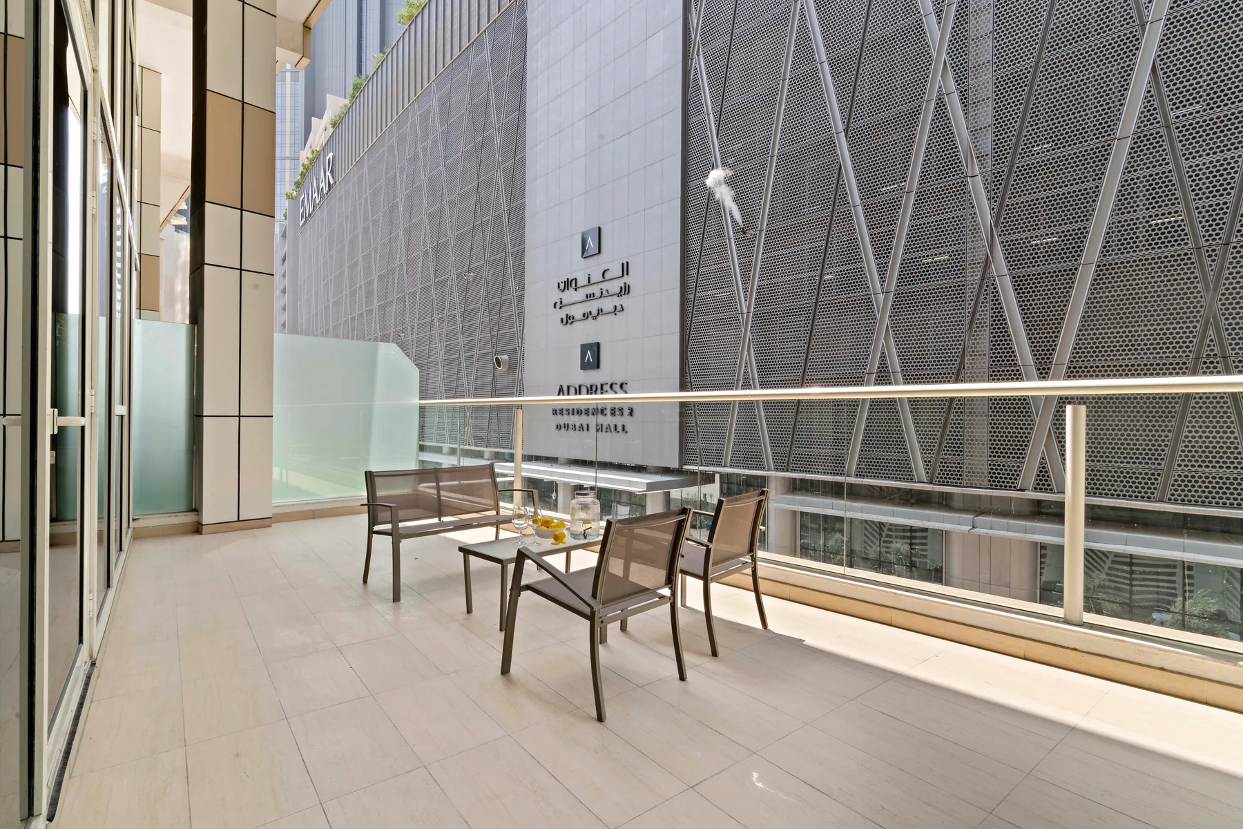 Una terraza exterior con asientos y una barandilla de vidrio junto a un edificio alto.