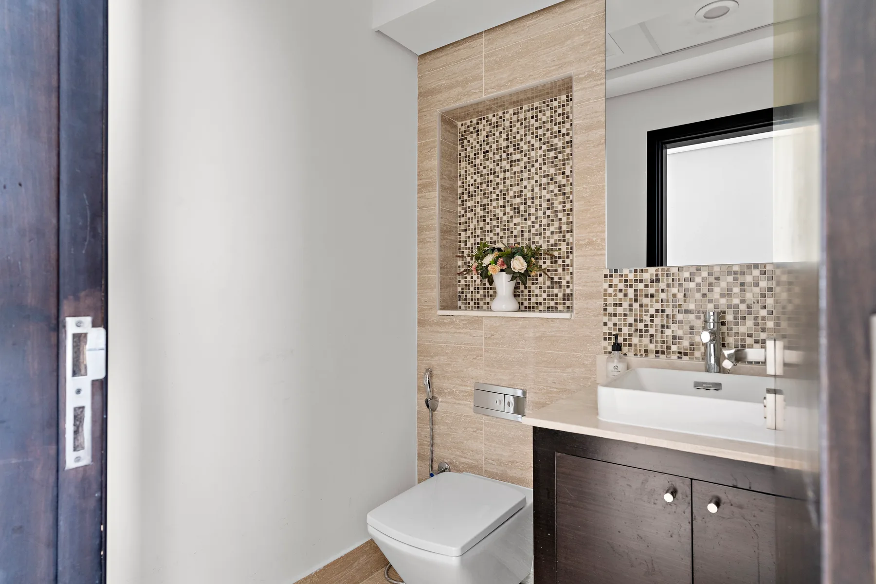 Un baño moderno con lavabo de pared e inodoro junto a paredes revestidas con azulejos.