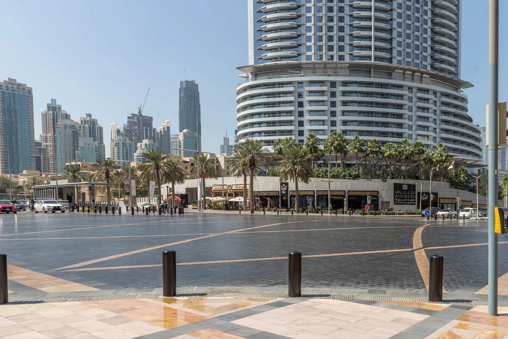 Una plaza pavimentada abierta da a un edificio alto curvo y locales junto a palmeras.
