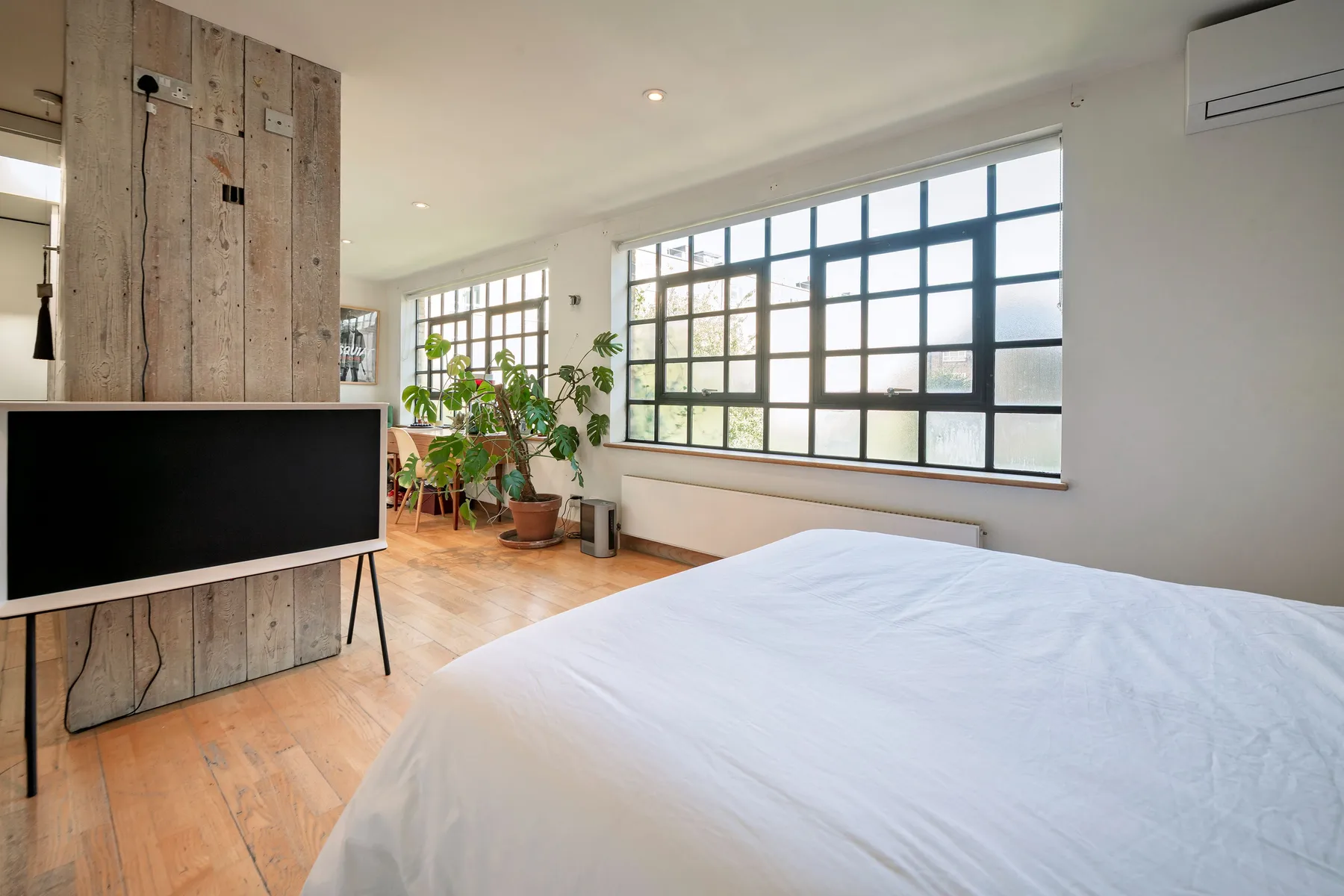 Un dormitorio luminoso con una cama grande, amplias ventanas y varias plantas en macetas.