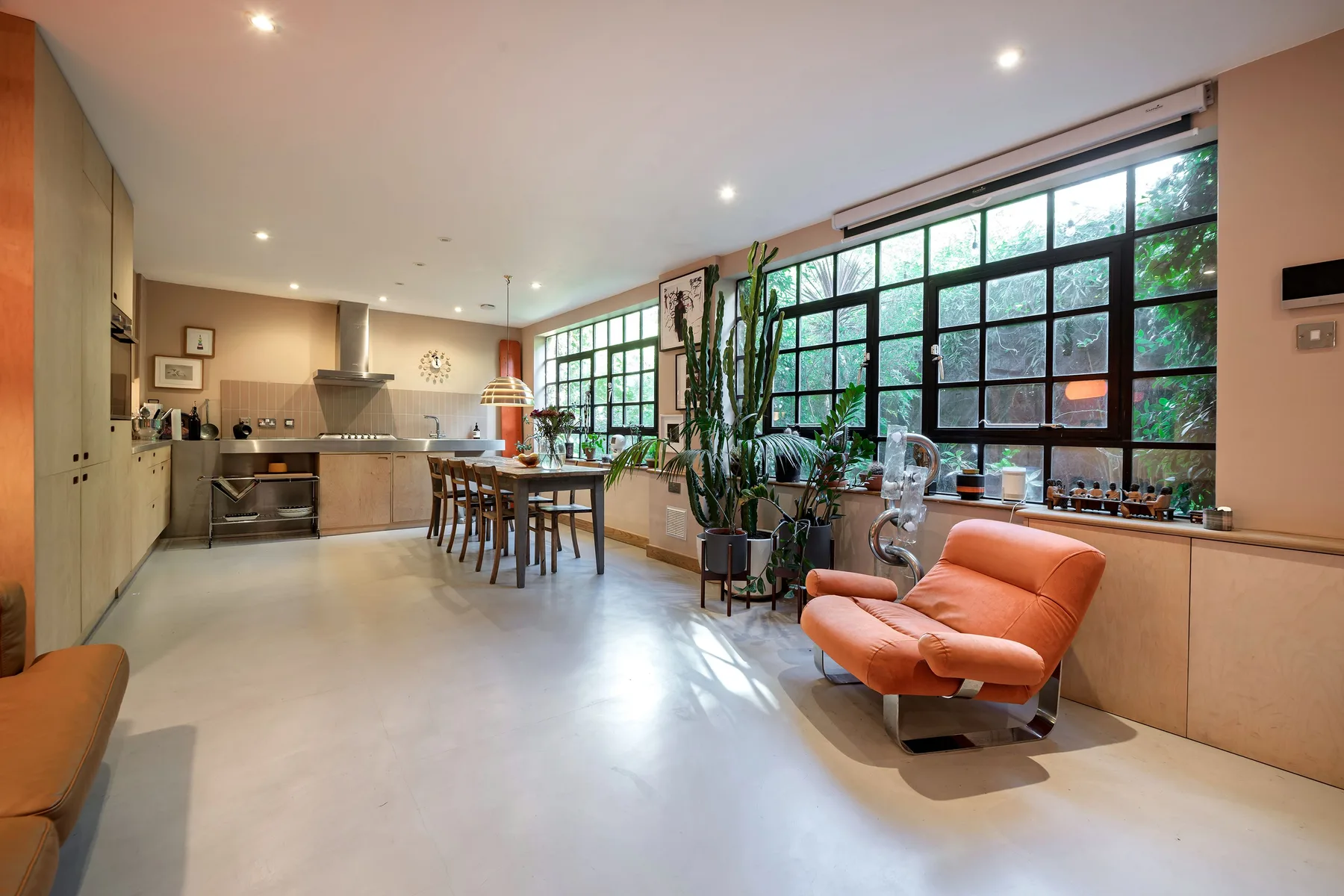 Una amplia cocina y comedor se abre junto a grandes ventanas con marcos negros.