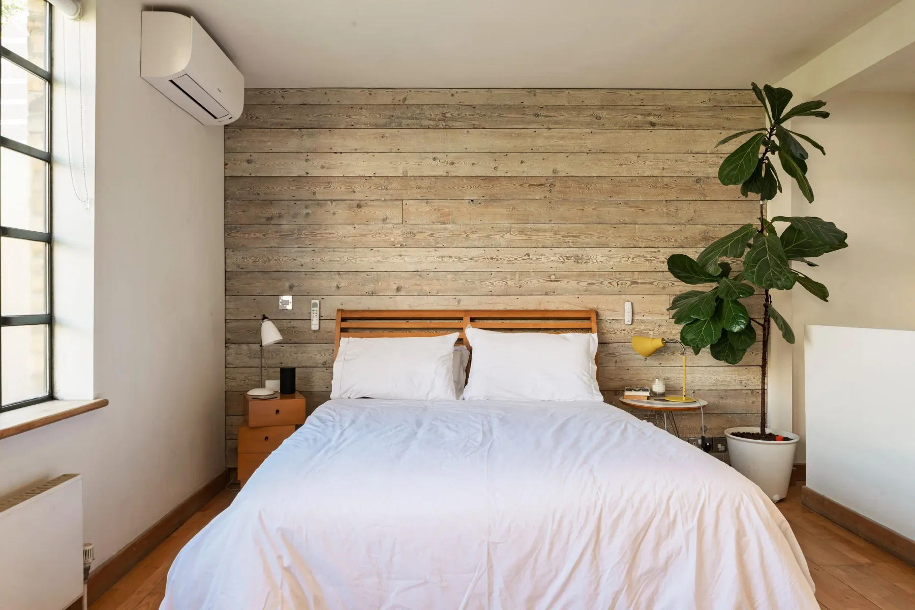 Un dormitorio con una cama, mesitas de noche y una planta alta.