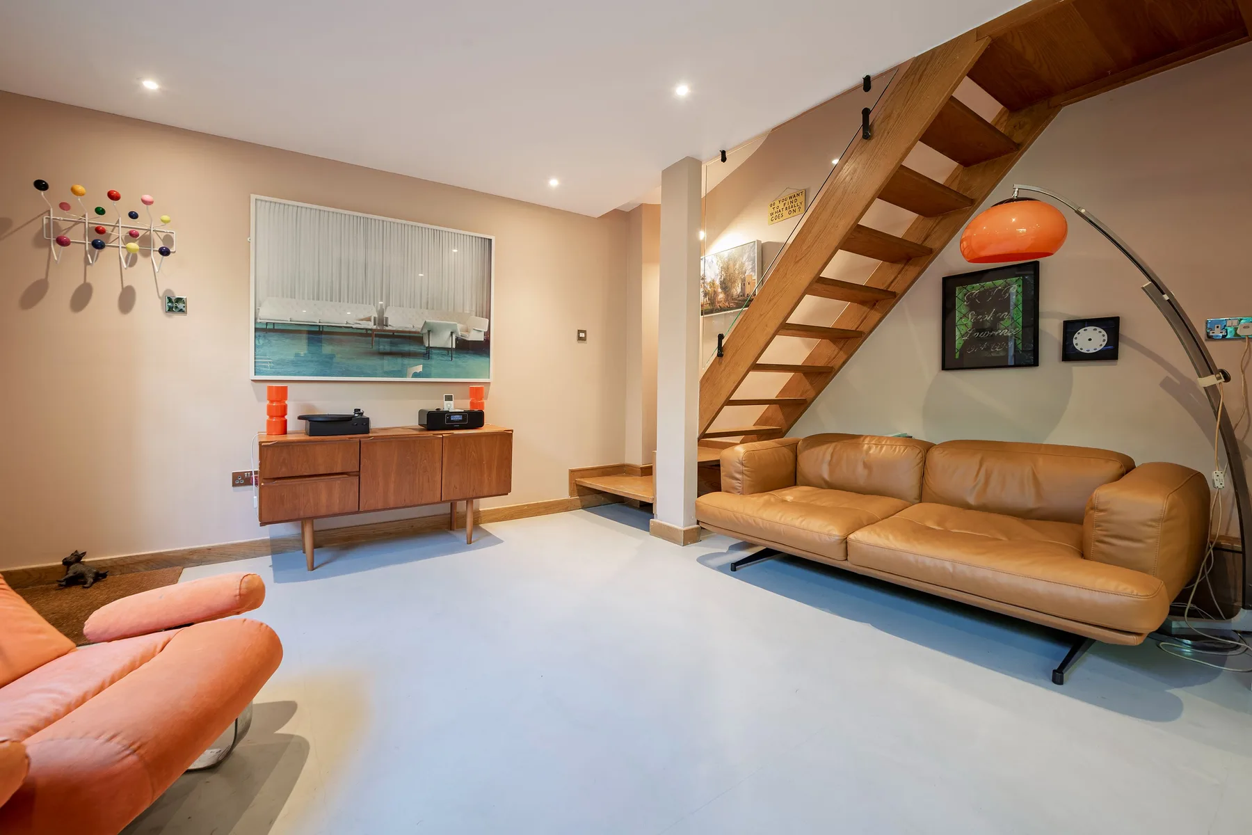 Una sala de estar con asientos color canela bajo una escalera de madera.