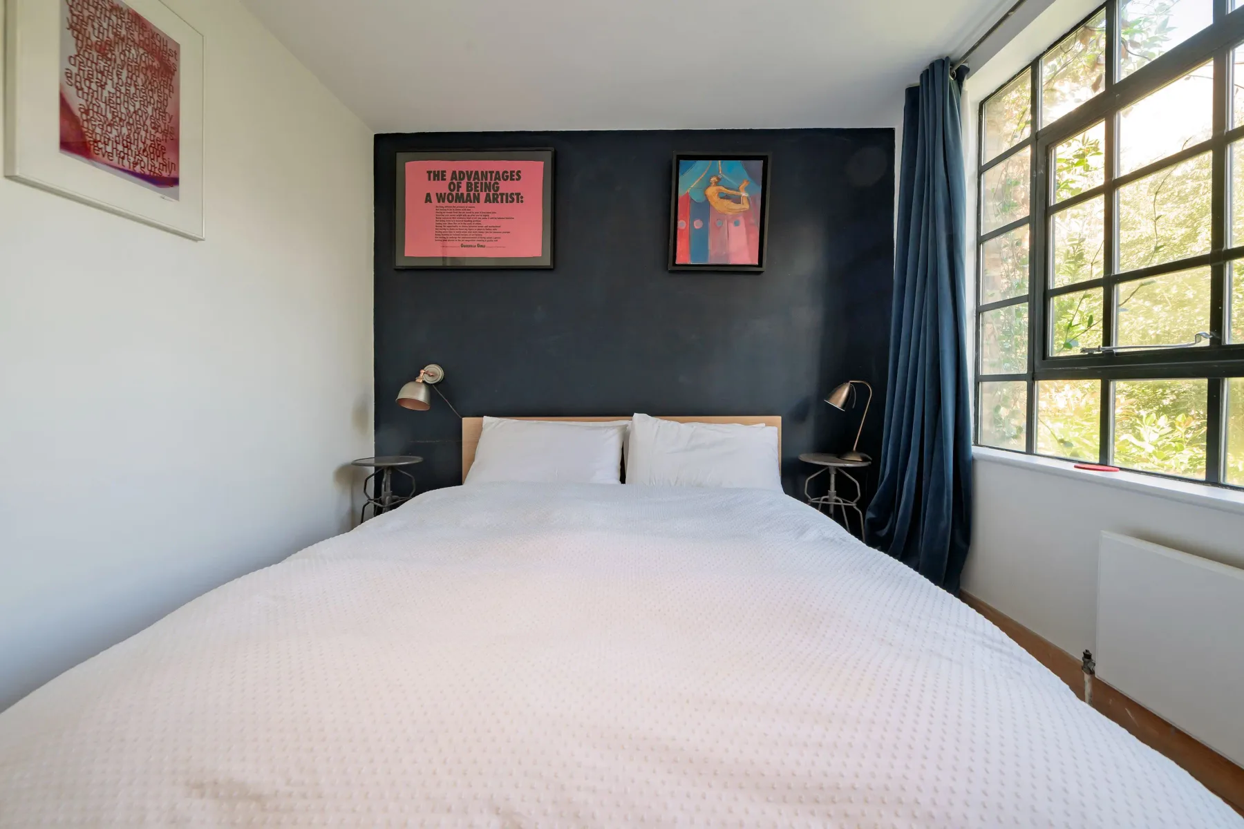 Un dormitorio con una cama bajo cuadros enmarcados y junto a una ventana amplia.