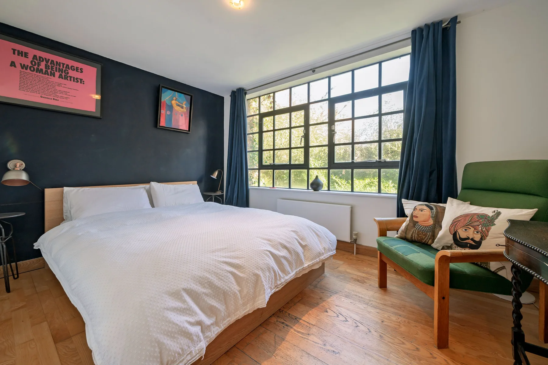 Un dormitorio con una cama grande junto a un sillón verde y una amplia ventana.