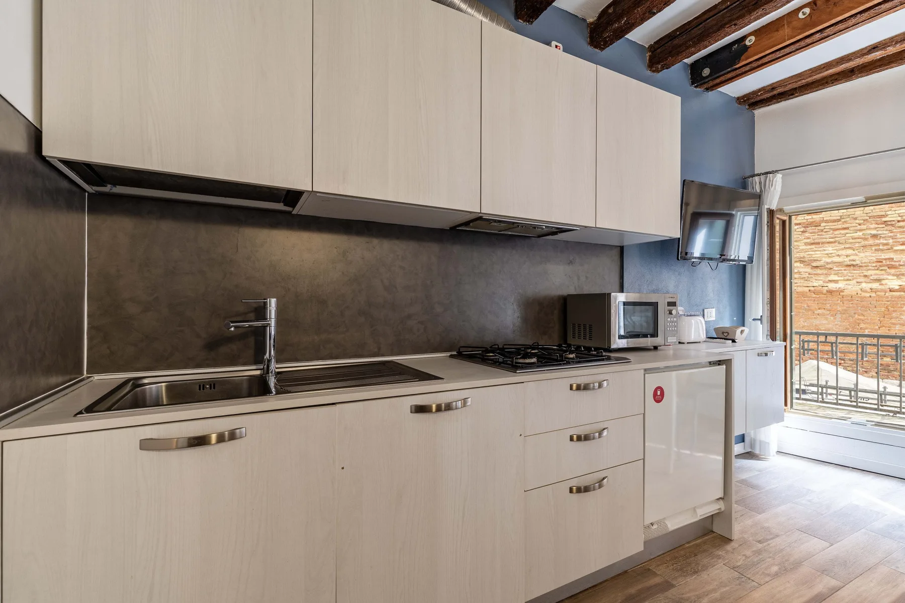 A modern kitchen with a long counter, sink, cooktop, and light cabinetry.