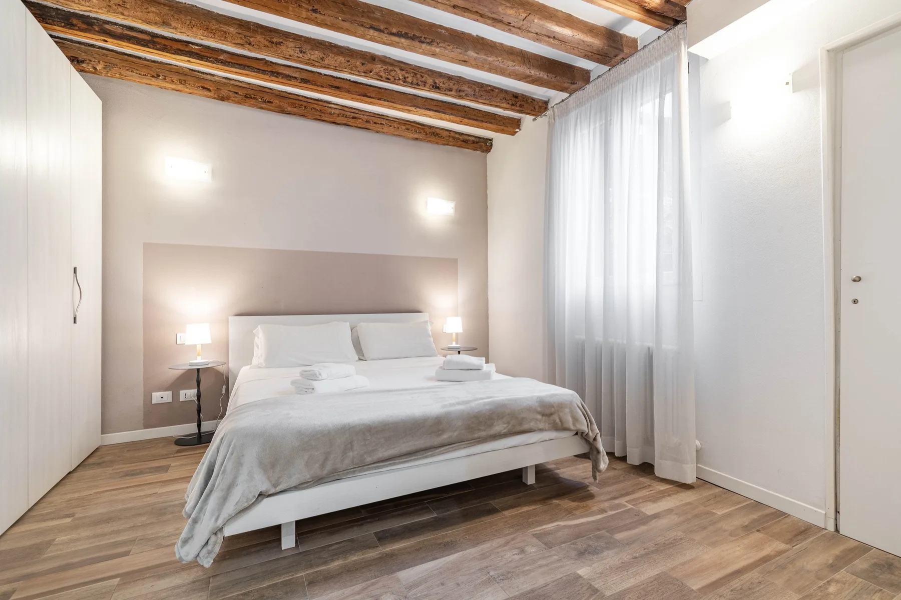 A bedroom with a bed, bedside lamps, and exposed wooden ceiling beams.