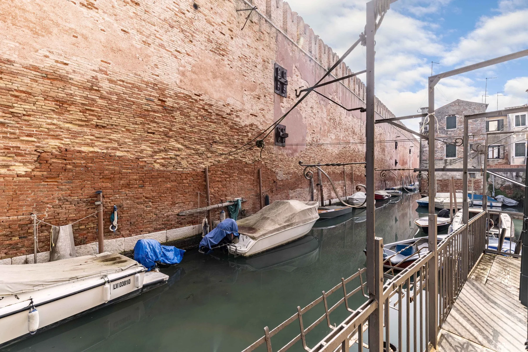A narrow canal runs beside a brick wall and a raised pedestrian walkway.