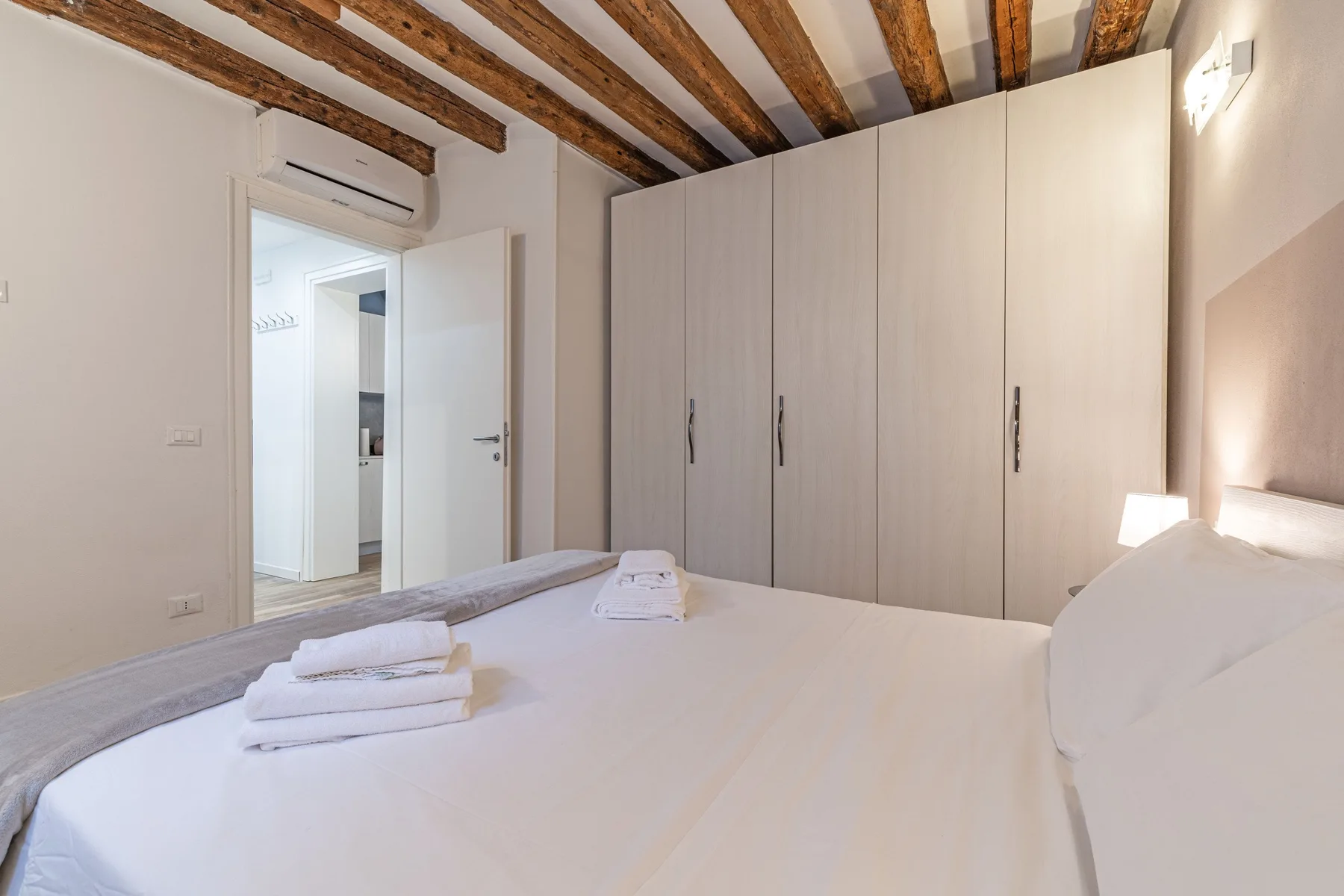 A bright bedroom with a bed, folded towels, and a large wardrobe.