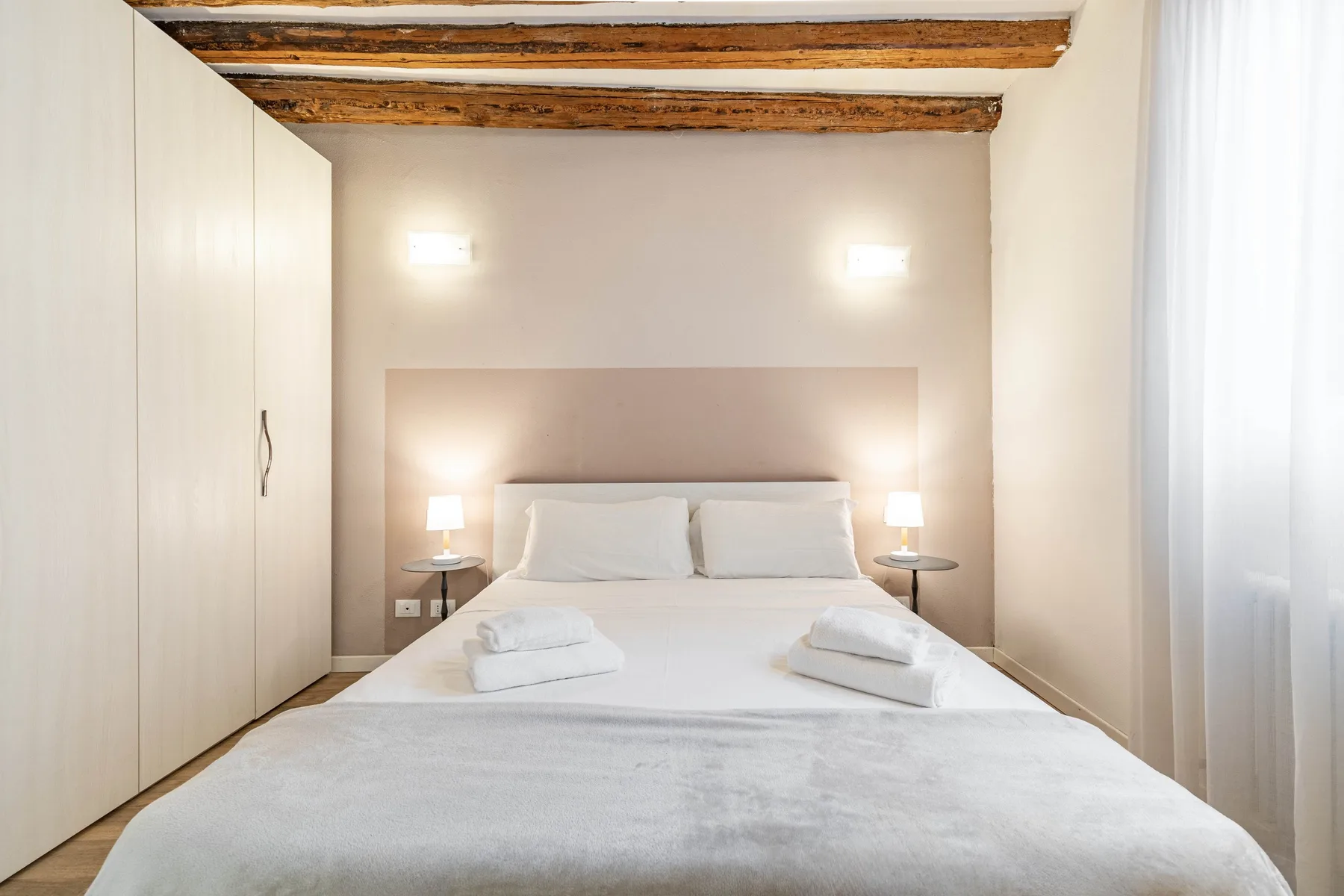A bright bedroom with a neatly made bed and bedside lamps.
