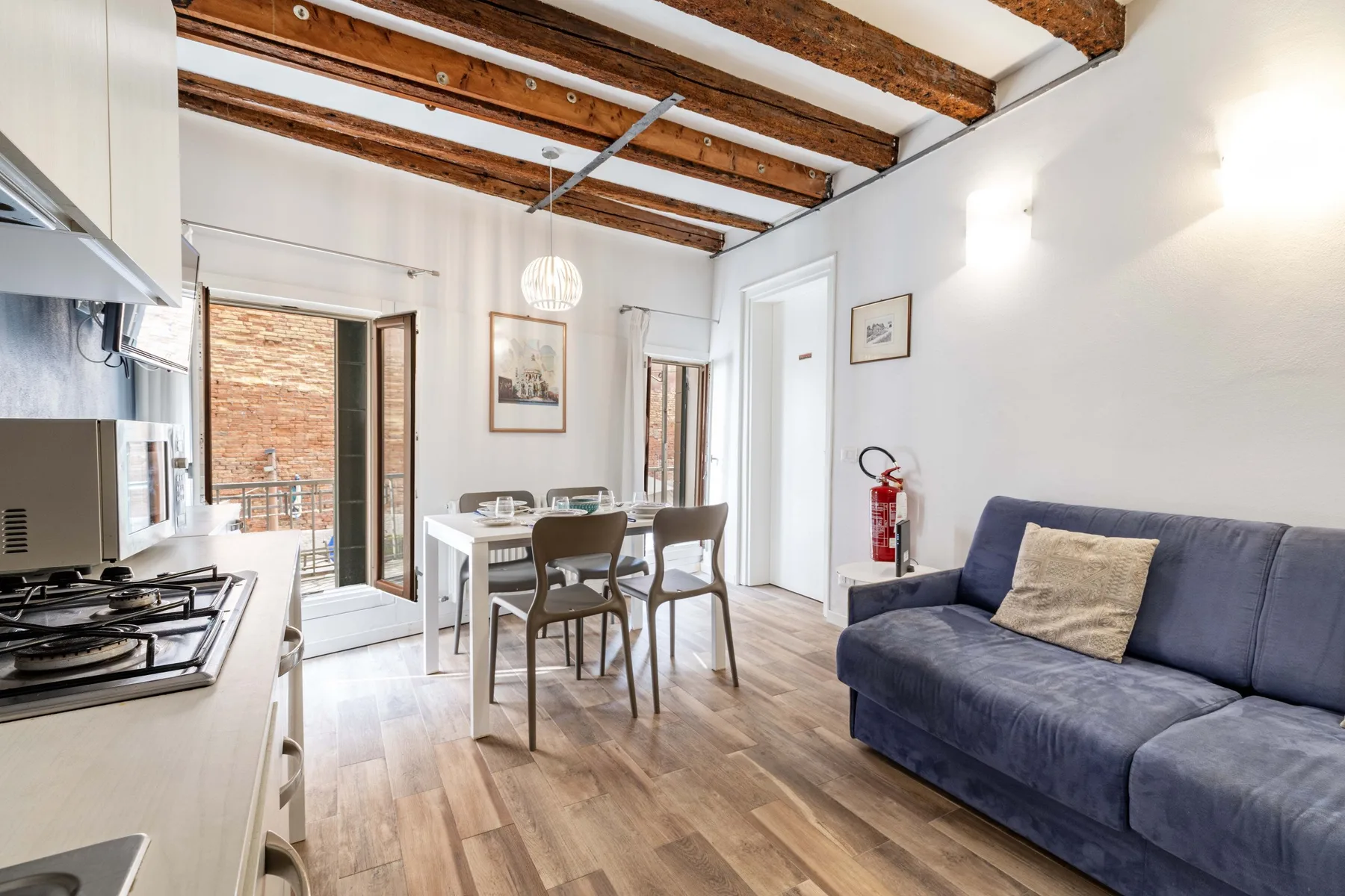 A bright living and dining area with a blue sofa and a table beneath exposed ceiling beams.