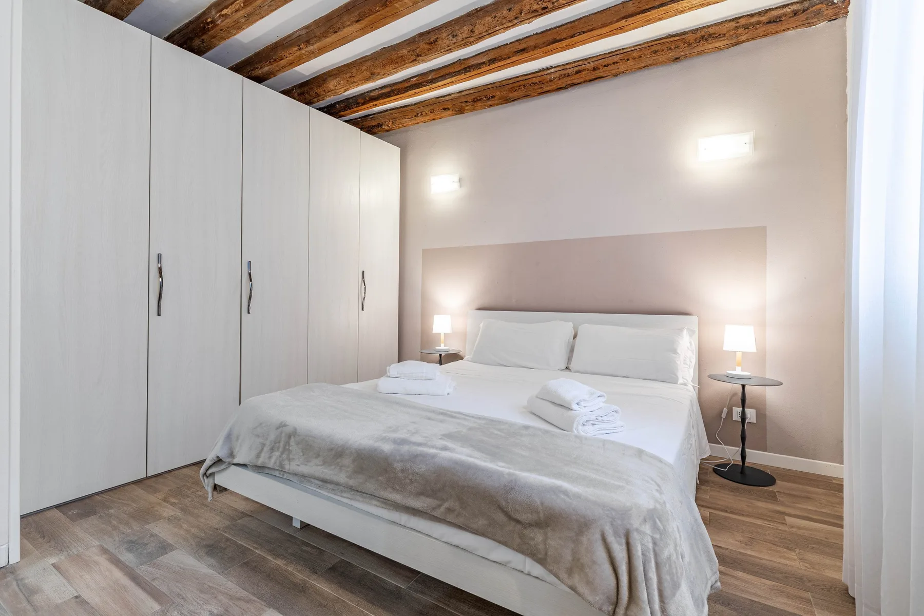 A bedroom with a neatly made bed, bedside tables, and a row of wardrobes.
