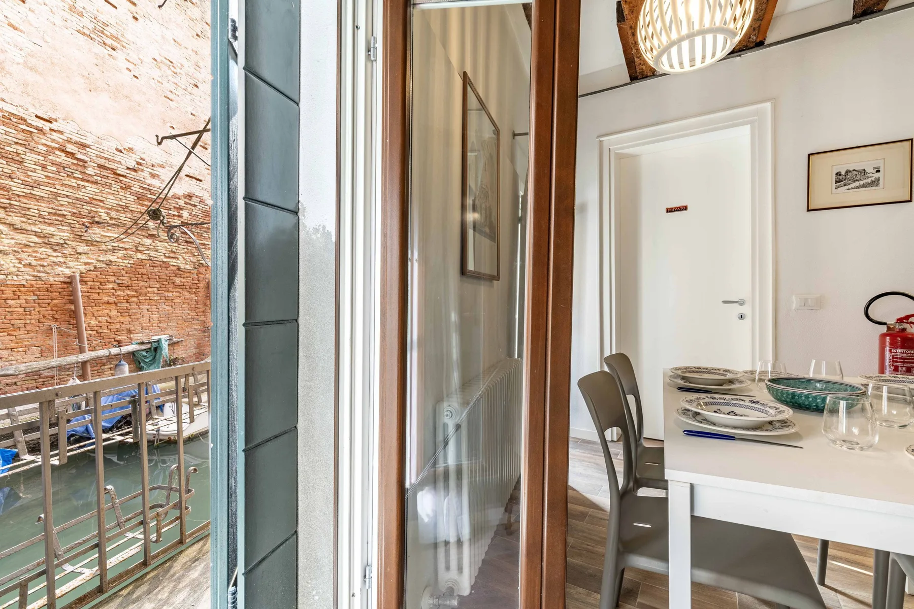 A dining area with a set table sits beside open doors overlooking a brick courtyard.