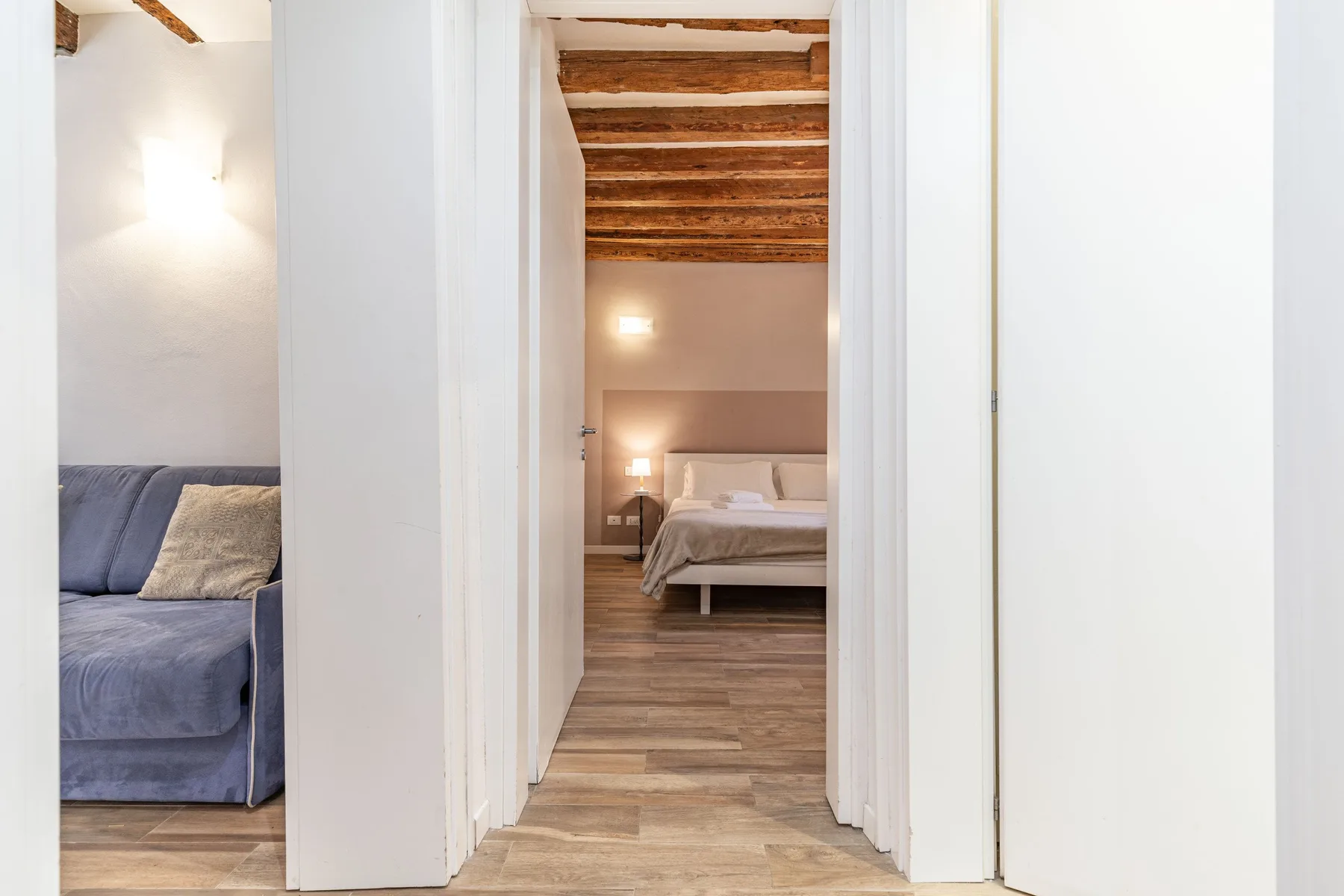A bedroom is visible through a hallway doorway, with a bed beneath exposed wooden ceiling beams.
