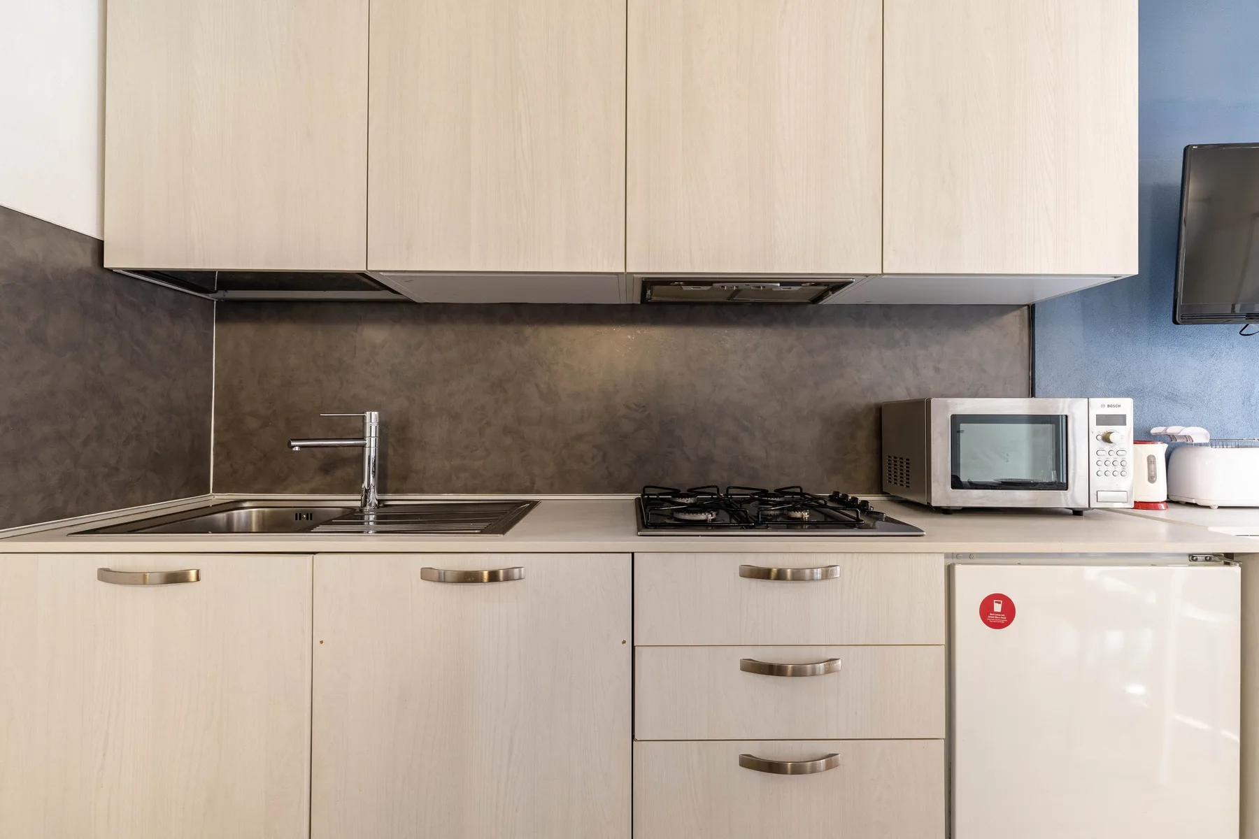 A modern kitchen with light cabinets, a sink, and a stovetop.